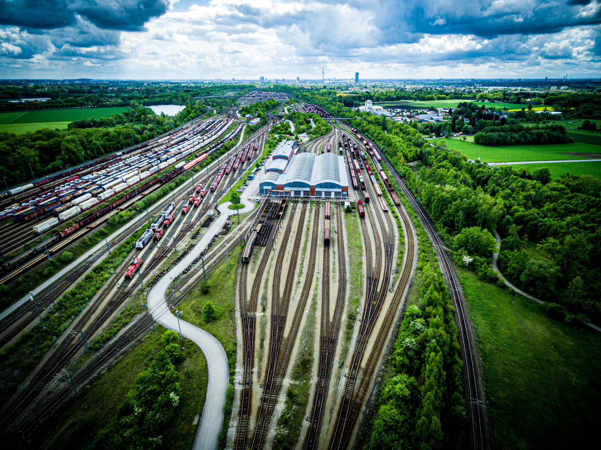 Aerial view of a large railway yard with multiple tracks, trains, and warehouses surrounded by green fields and forests.