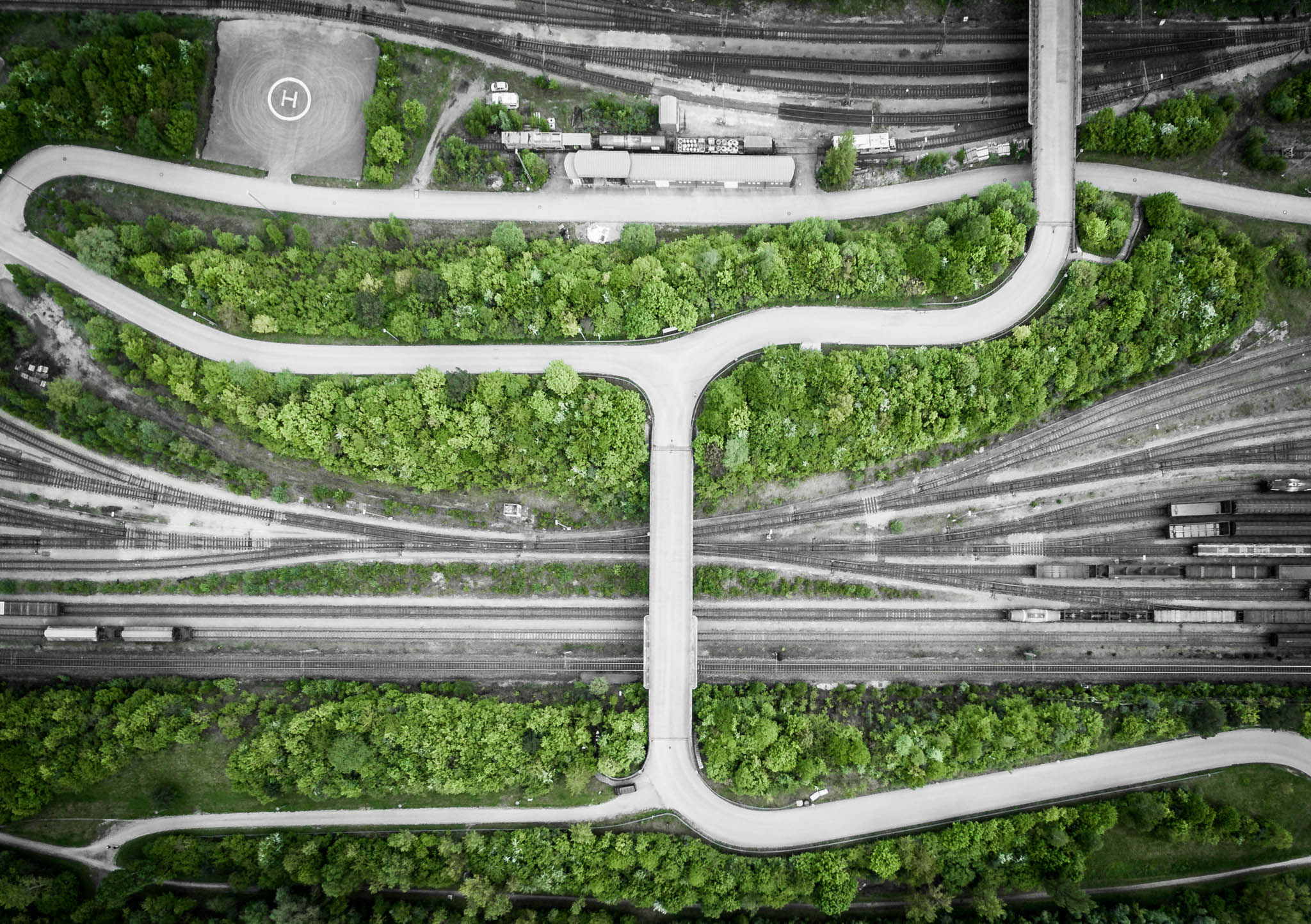 Aerial view of a lush green park intersected by roads and railway tracks, with a visible helipad on the top left.