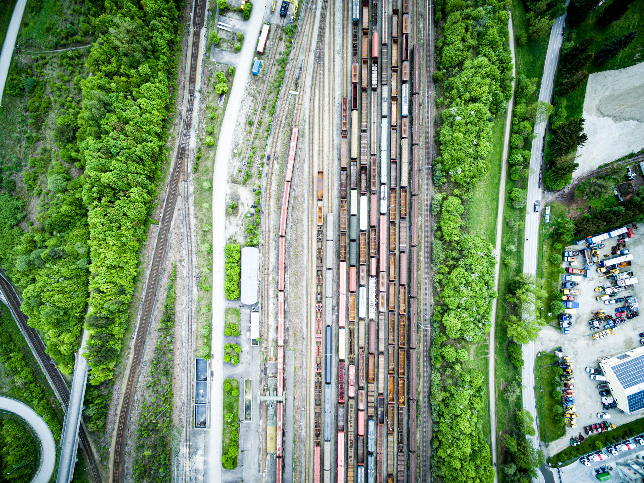 Aerial view of a train yard with multiple tracks and freight cars, surrounded by lush green trees and adjacent roads.
