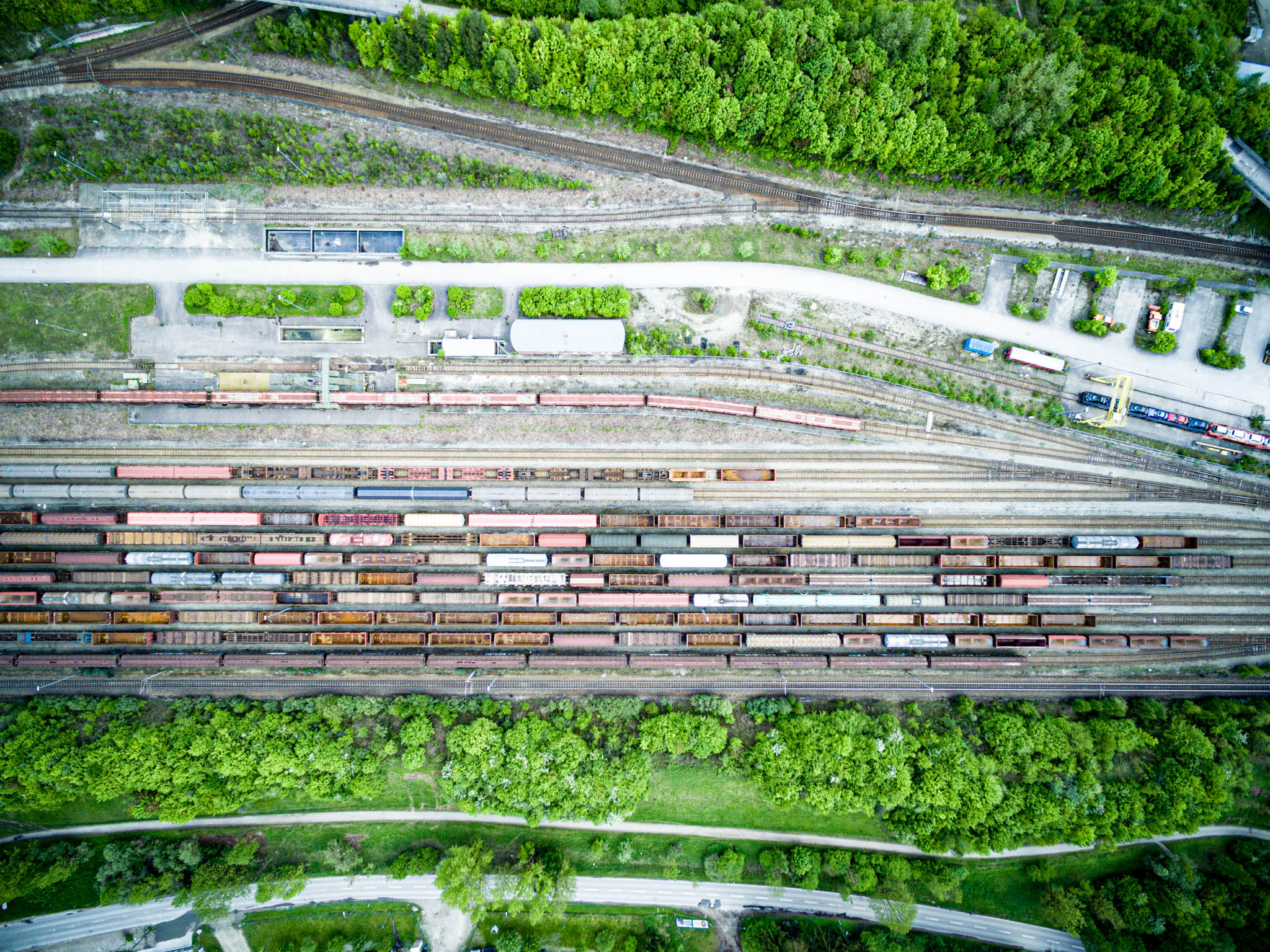 Aerial view of a busy railway yard with numerous freight trains and lush green trees surrounding the tracks.