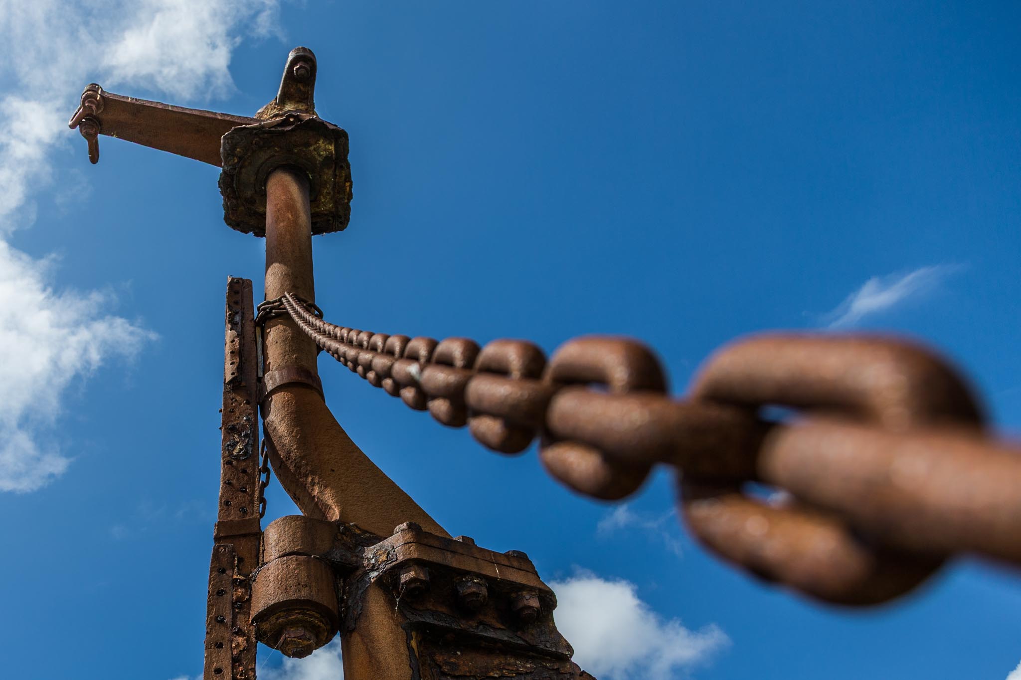Rusted chain and metal structure against blue sky with clouds in the background.