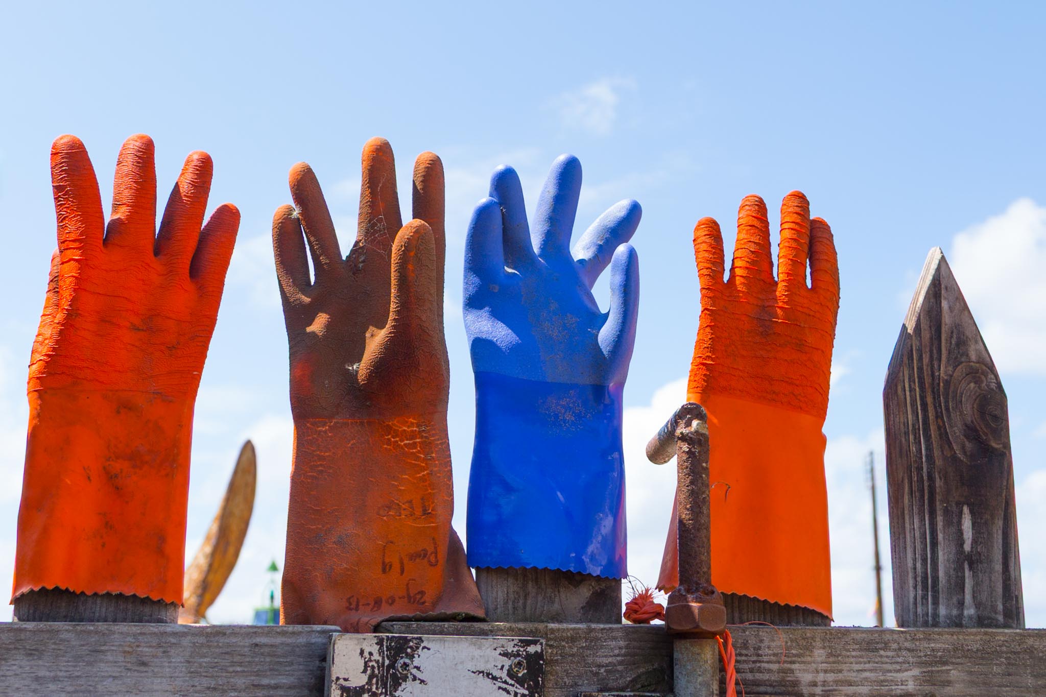 Colorful gloves drying on a wooden fence against a blue sky background.