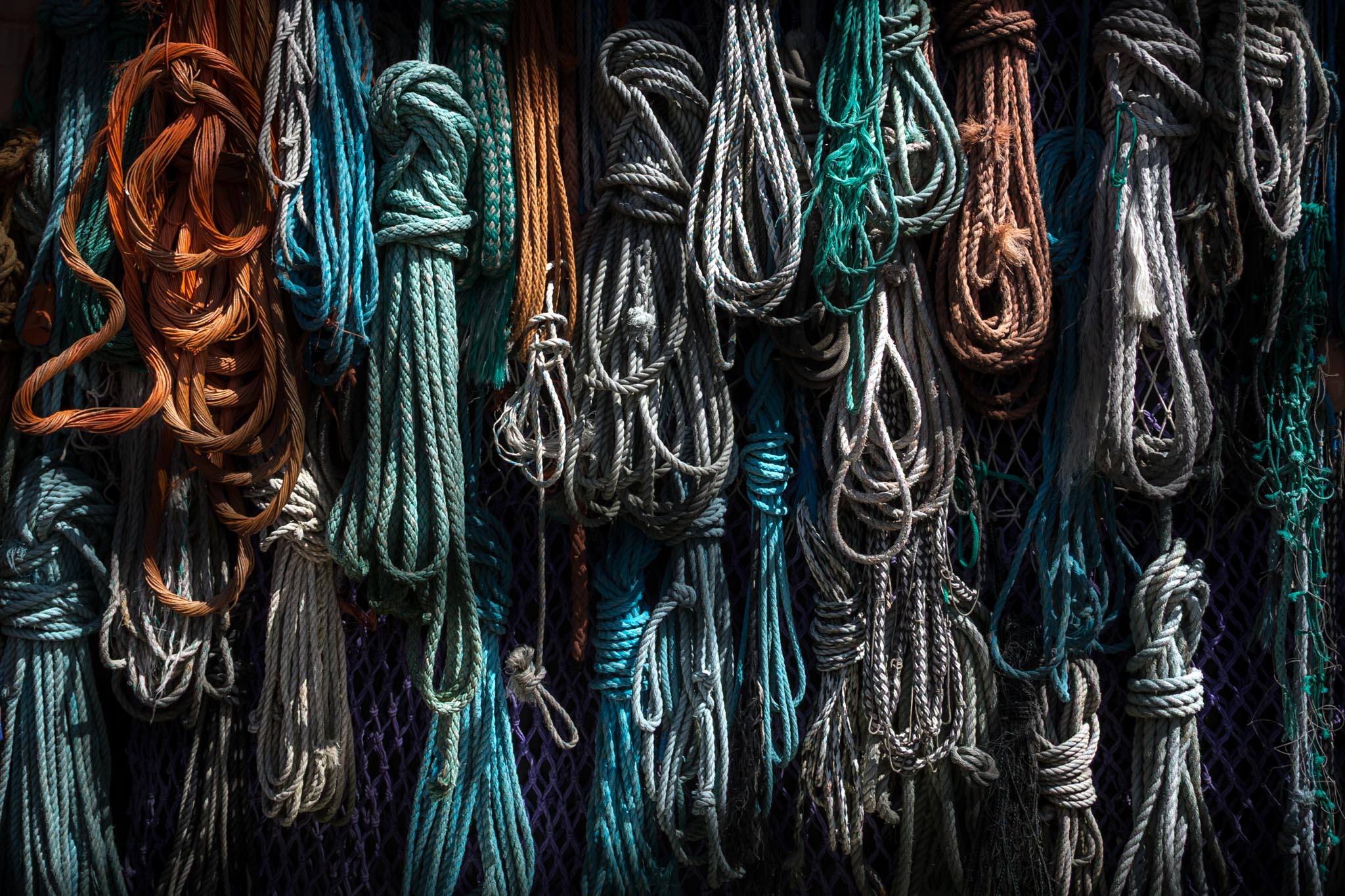Colorful nautical ropes hanging against a dark background, showcasing various textures and knots.