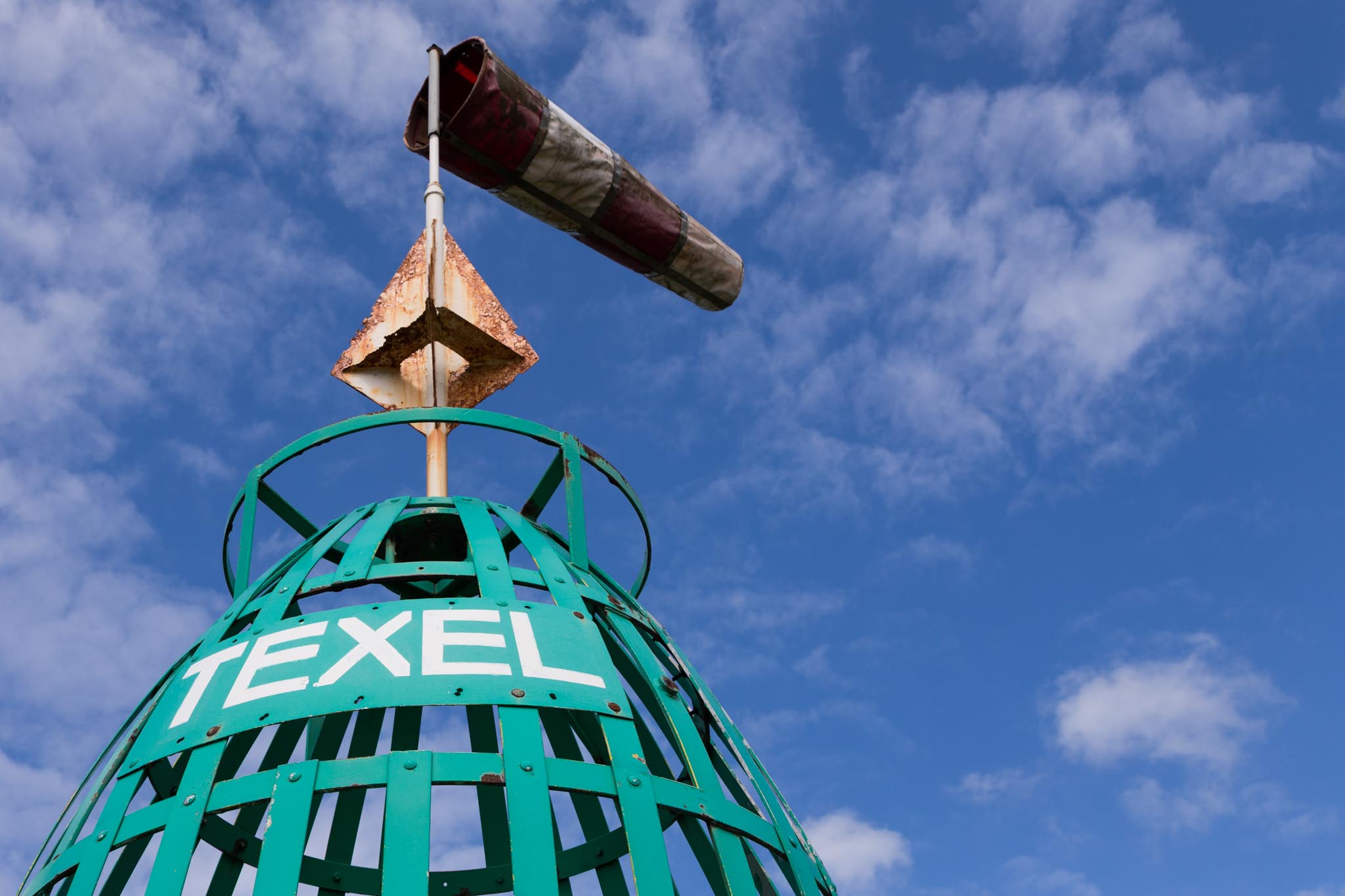 Green Texel buoy with a windsock against a blue sky with scattered clouds.