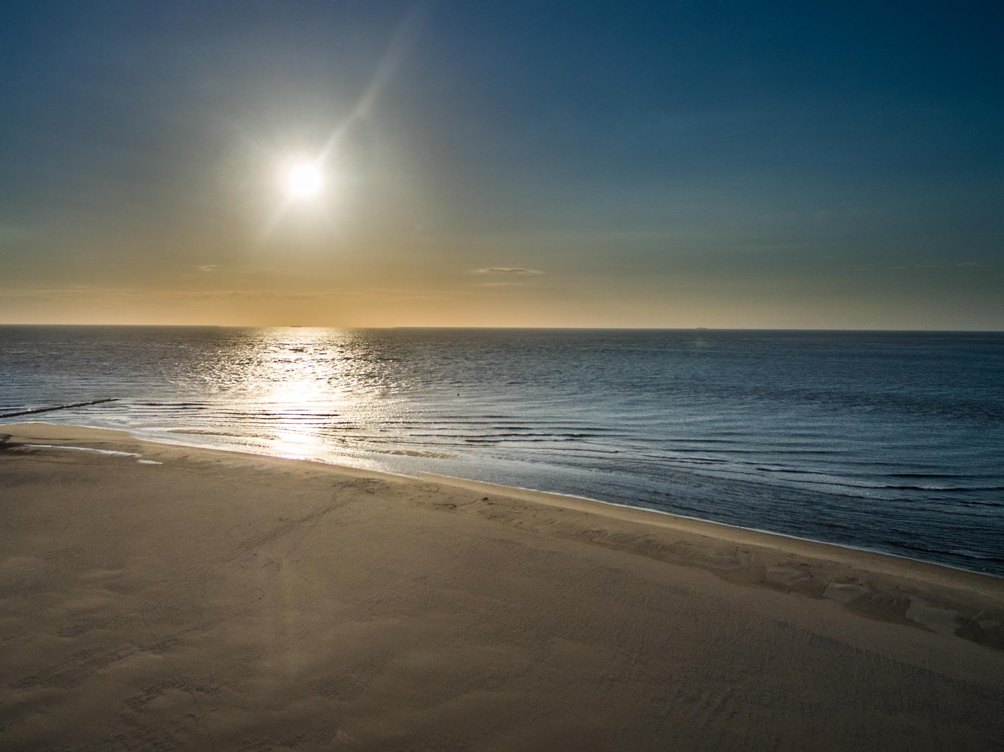 Sunrise over a calm ocean with gentle waves touching a sandy beach.