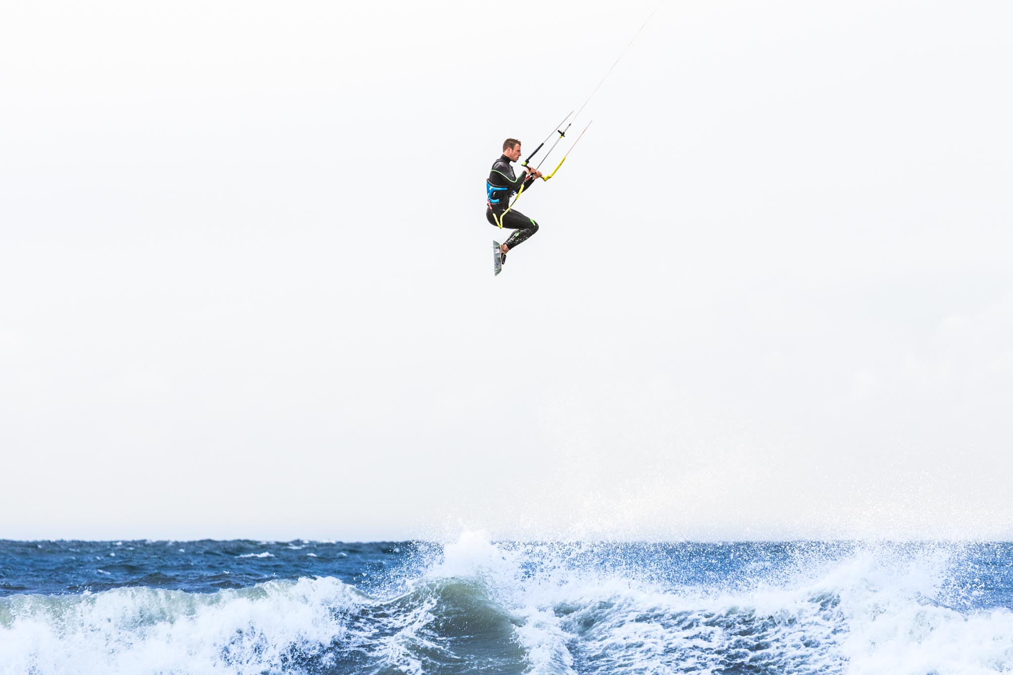 Kitesurfer jumping above ocean waves on a windy day with a clear sky background.
