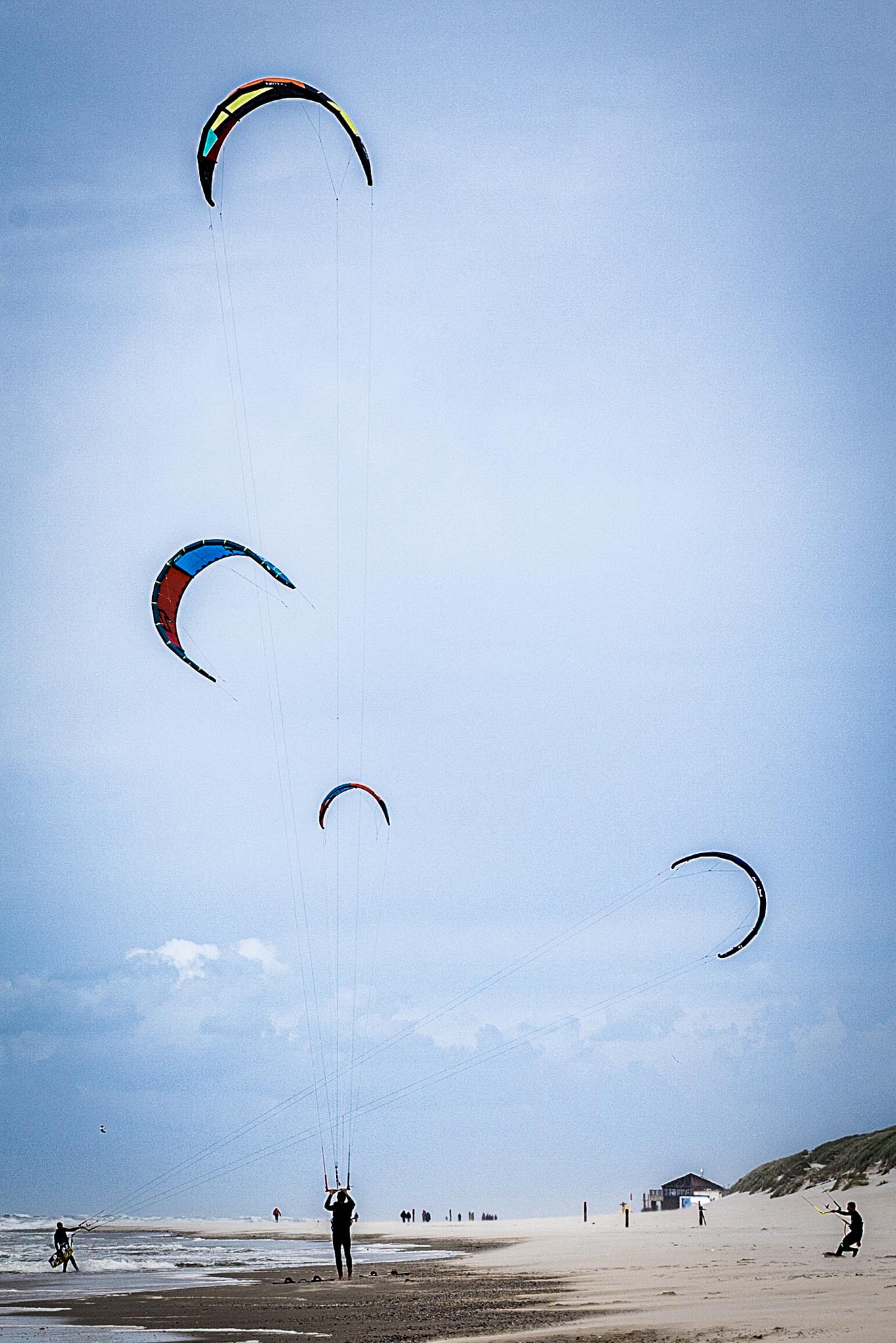Kite surfers on a windy beach with colorful kites in the sky under a clear blue sky.