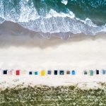 Exploring Texel Island – Family Trip to the Dutch Wadden Sea Aerial view of colorful beach huts lined up on a sandy beach with waves crashing ashore.