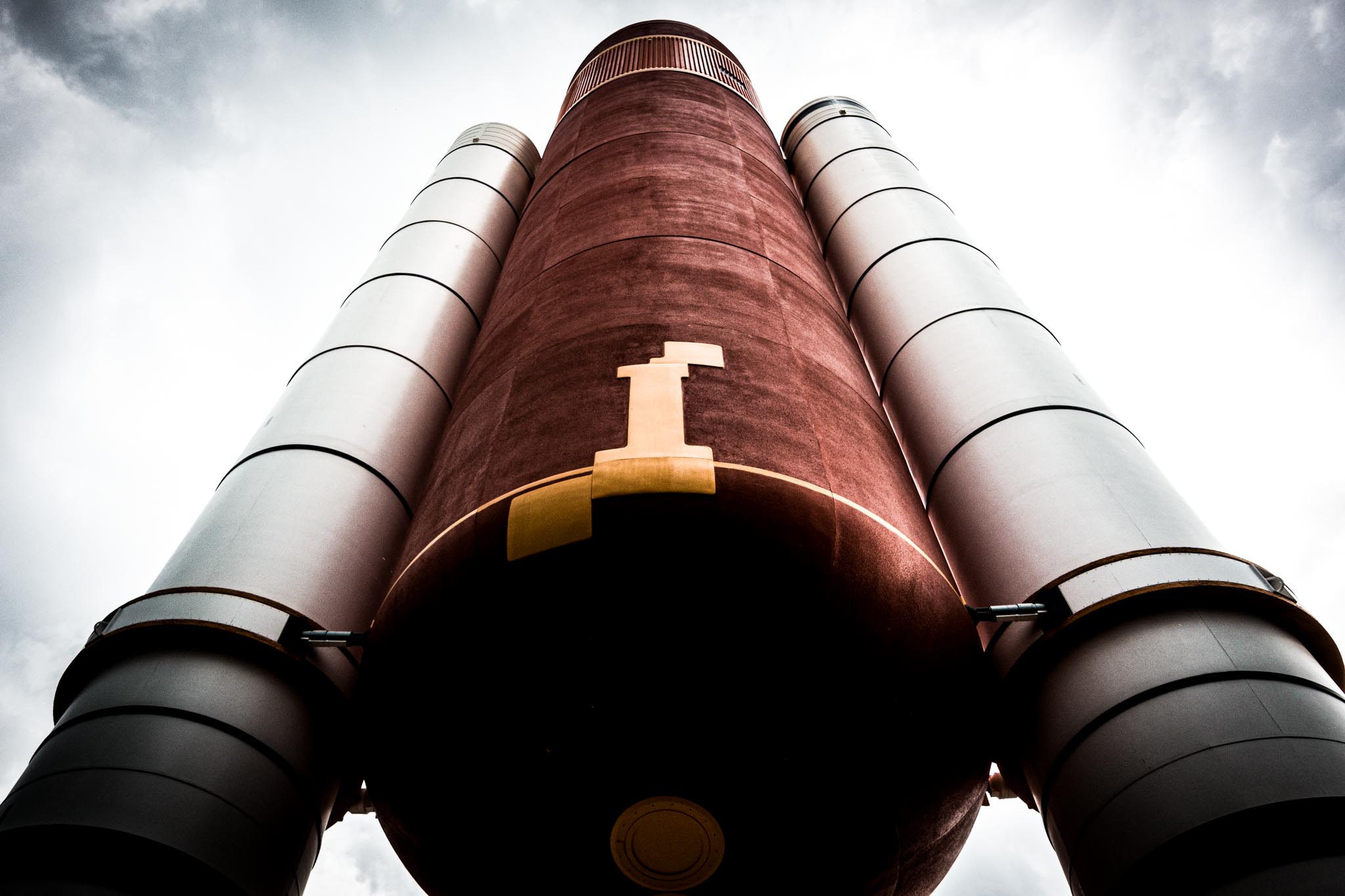 Low-angle view of a rocket's main fuel tank and boosters against a cloudy sky.