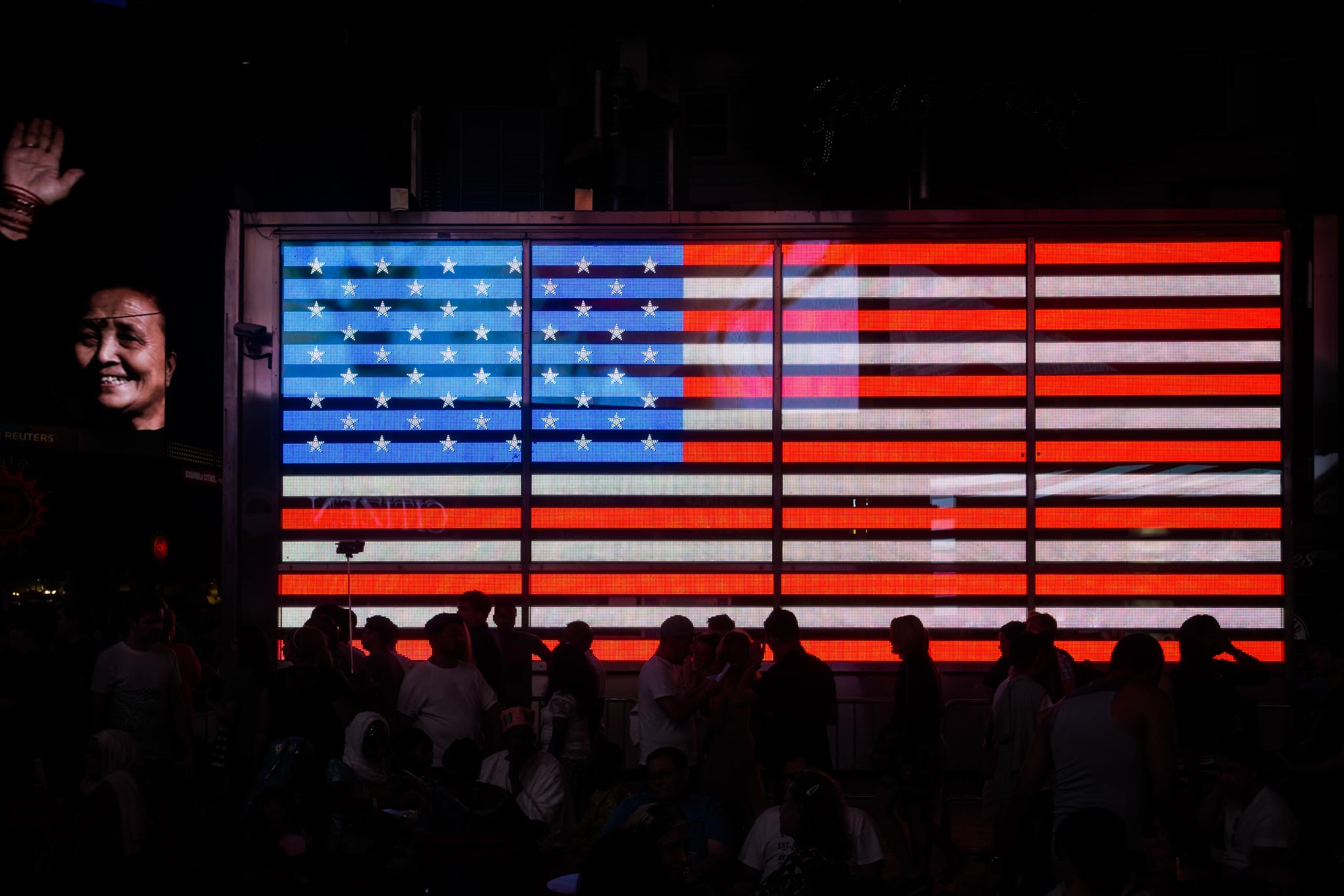 Silhouetted crowd in front of an illuminated American flag display at night.