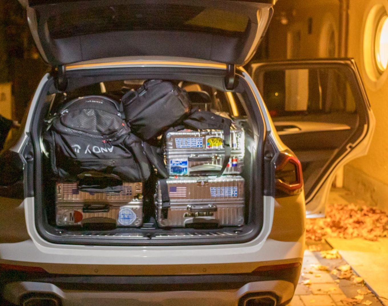 Open SUV trunk packed with luggage at night, person standing beside, leaves on ground.