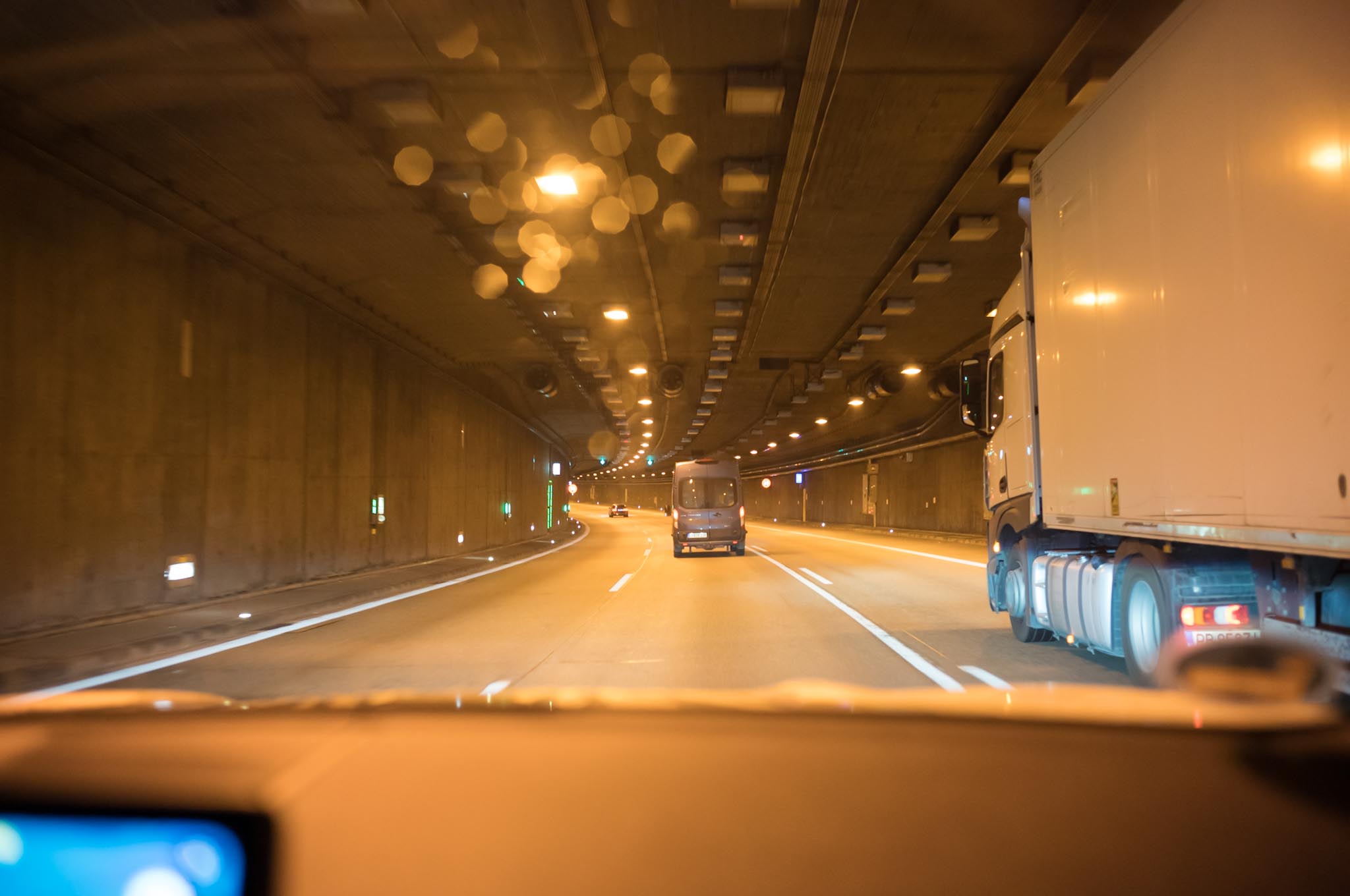 Driving inside a lit tunnel with vehicles including a truck and van, showing road lanes and tunnel ceiling infrastructure.