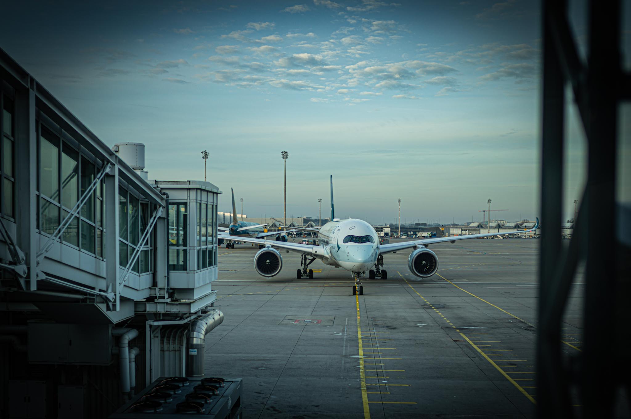 Airplane taxiing towards airport terminal gate under a cloudy sky at dawn.