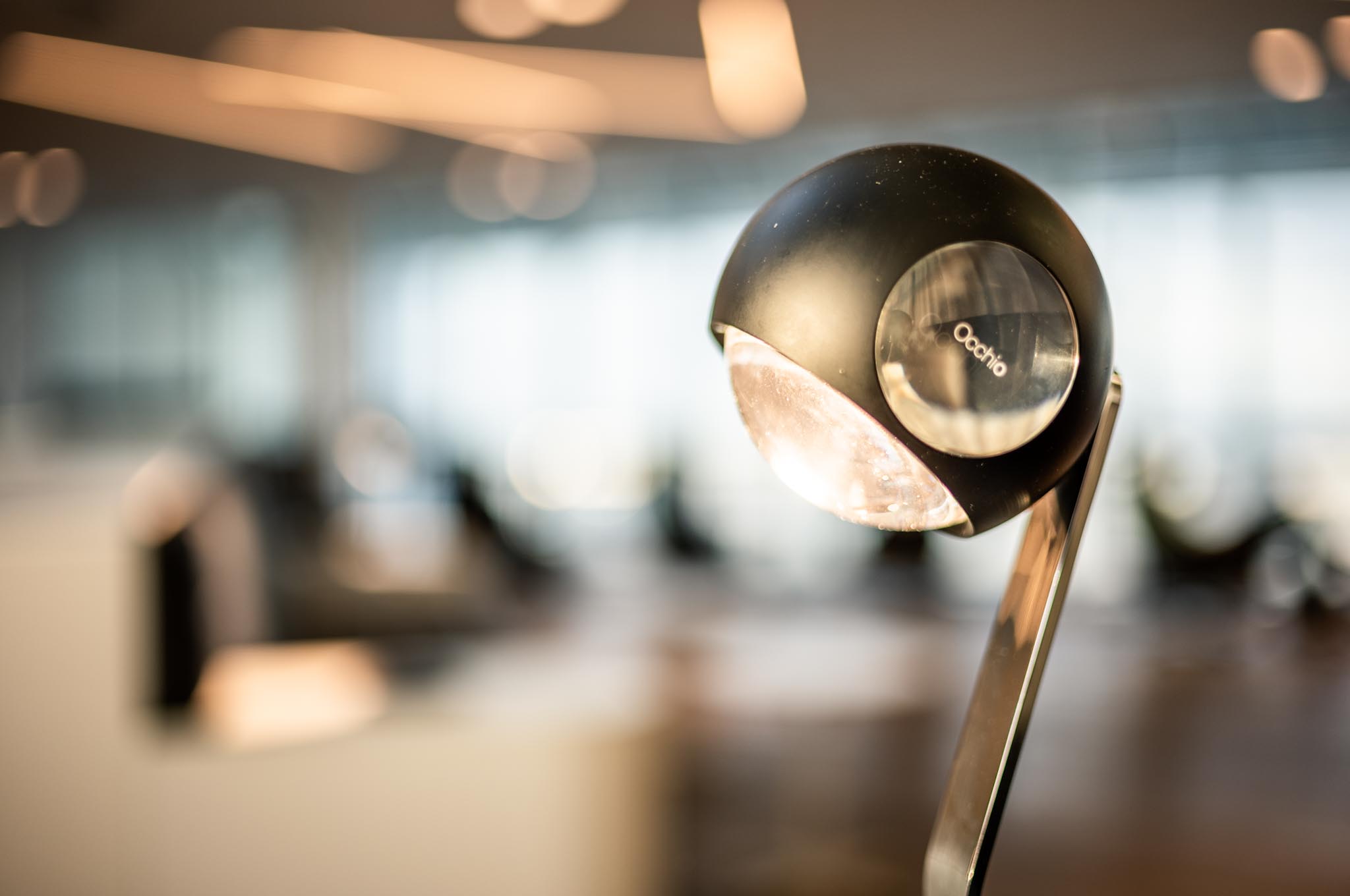 Modern black desk lamp in a blurred open office setting with natural light.