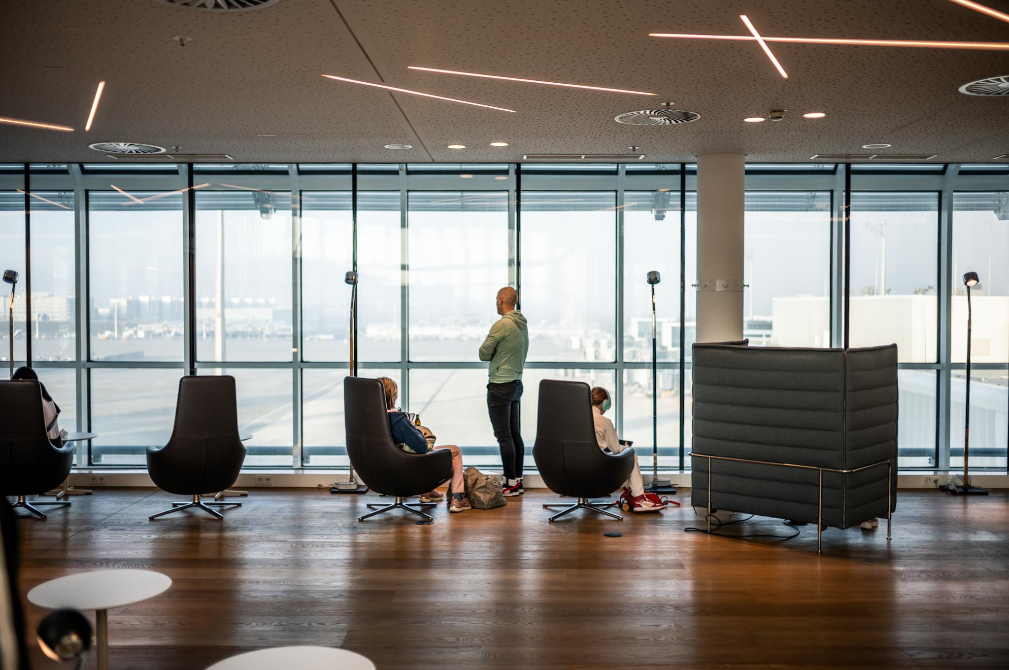 People relaxing and working in a modern airport lounge with large windows and stylish seating.