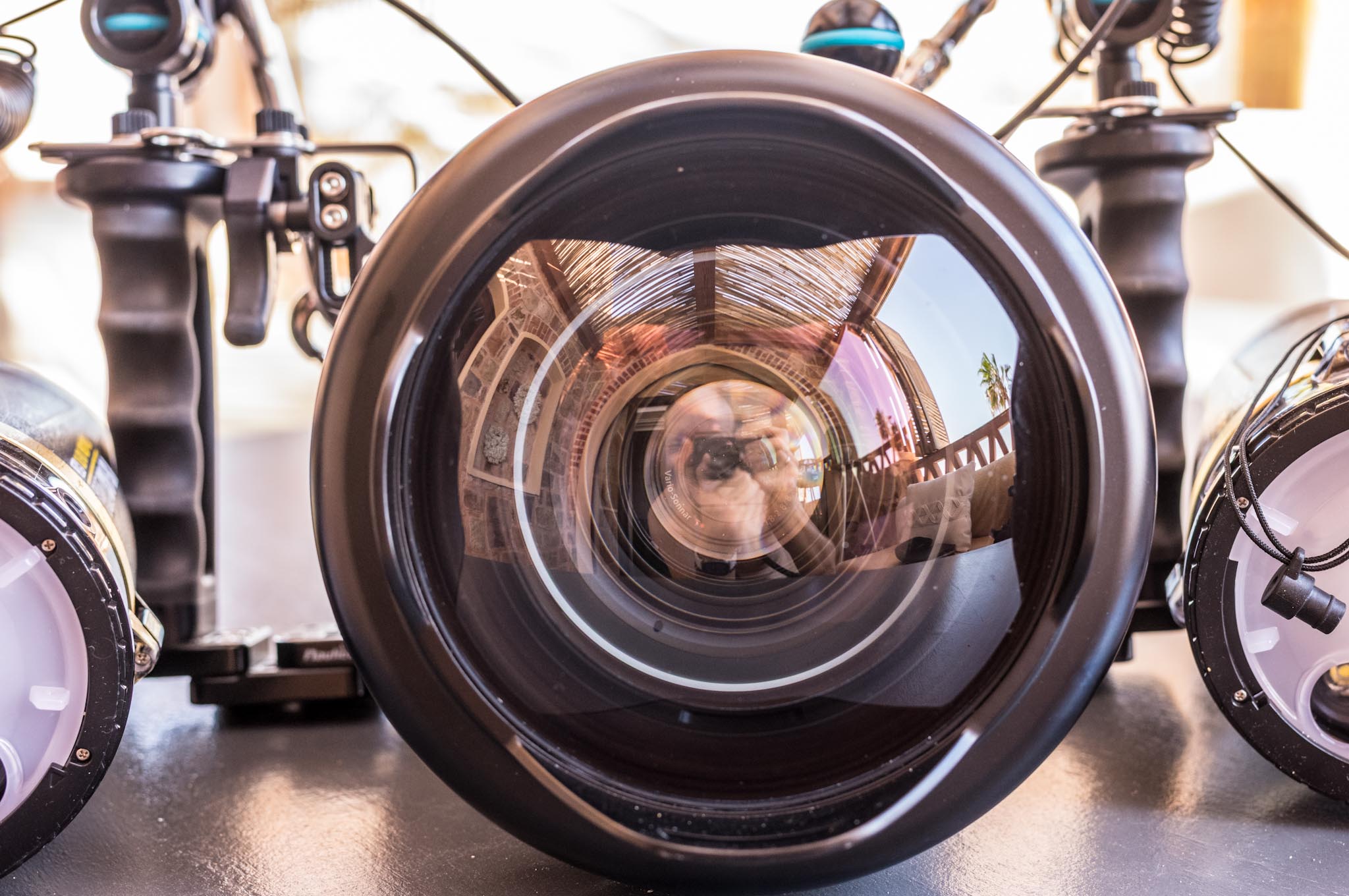 Close-up of a camera lens with intricate reflections of a photographer and a wooden structure.