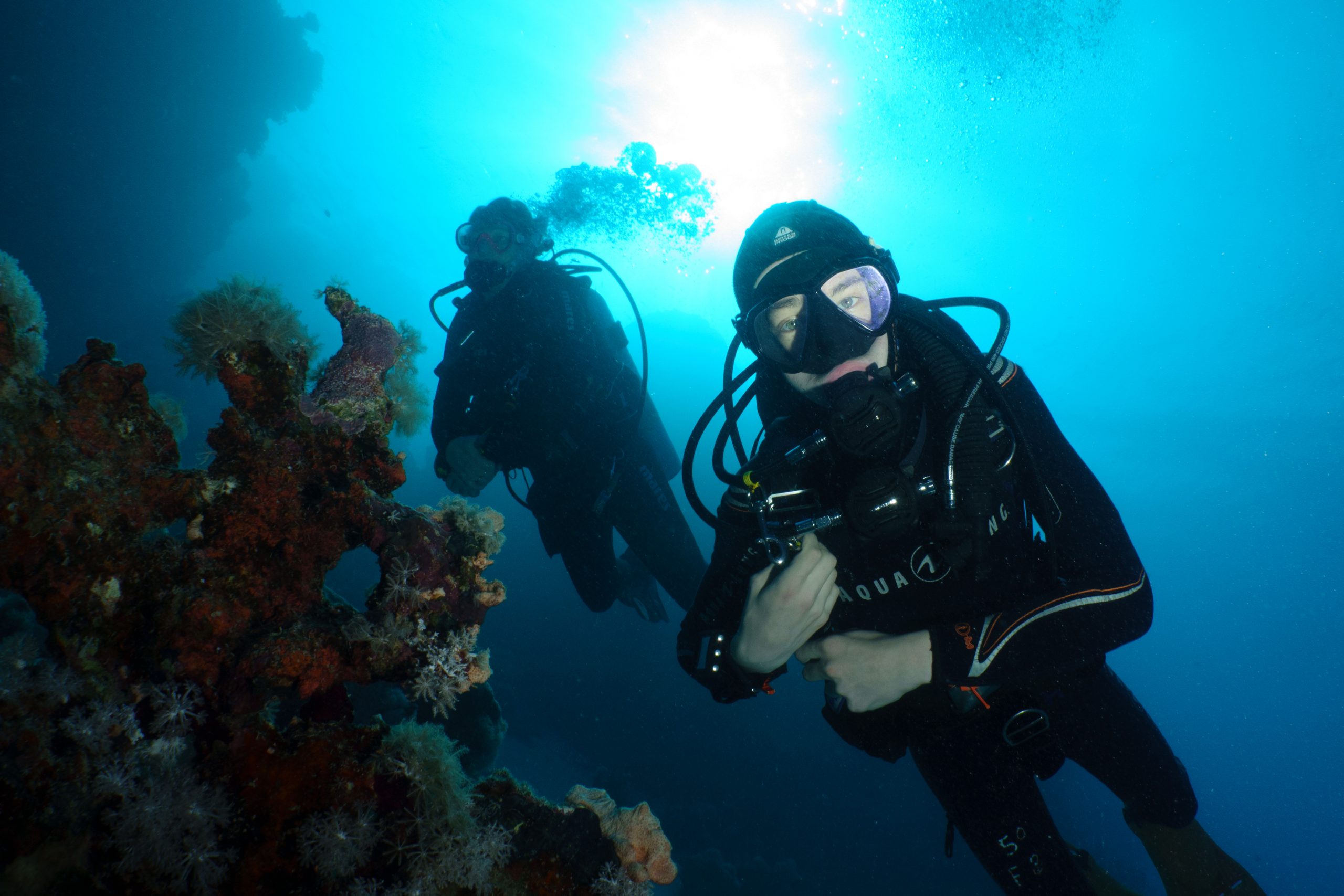 Two scuba divers exploring vibrant coral reef underwater with sunlight filtering through the ocean.