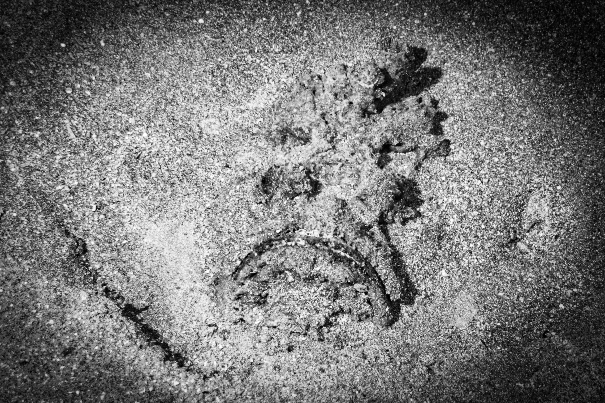Black and white image of a sad face drawn in sand, with a distinct downward-curved mouth and textured surface.