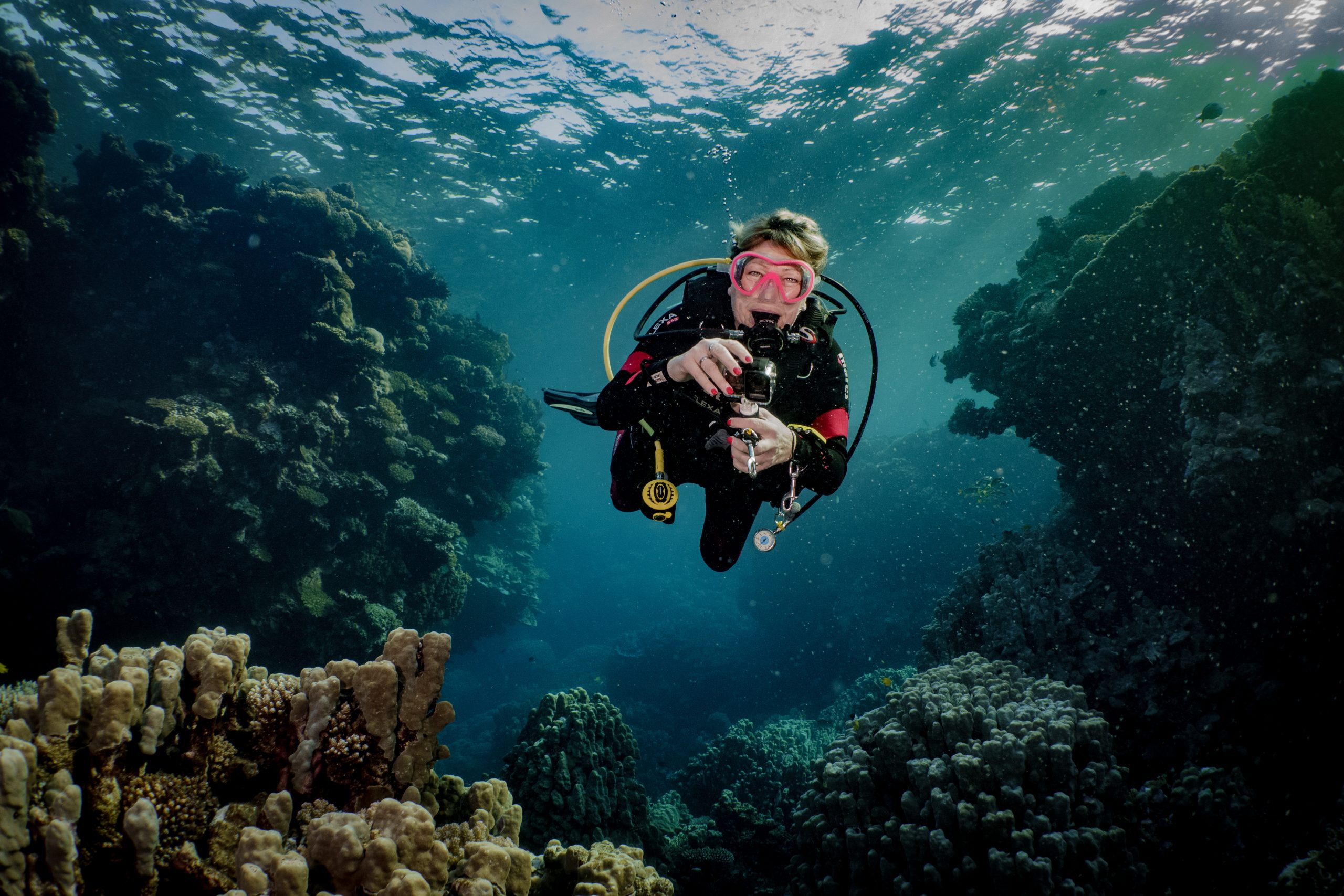 Scuba diver with camera exploring vibrant coral reef underwater.