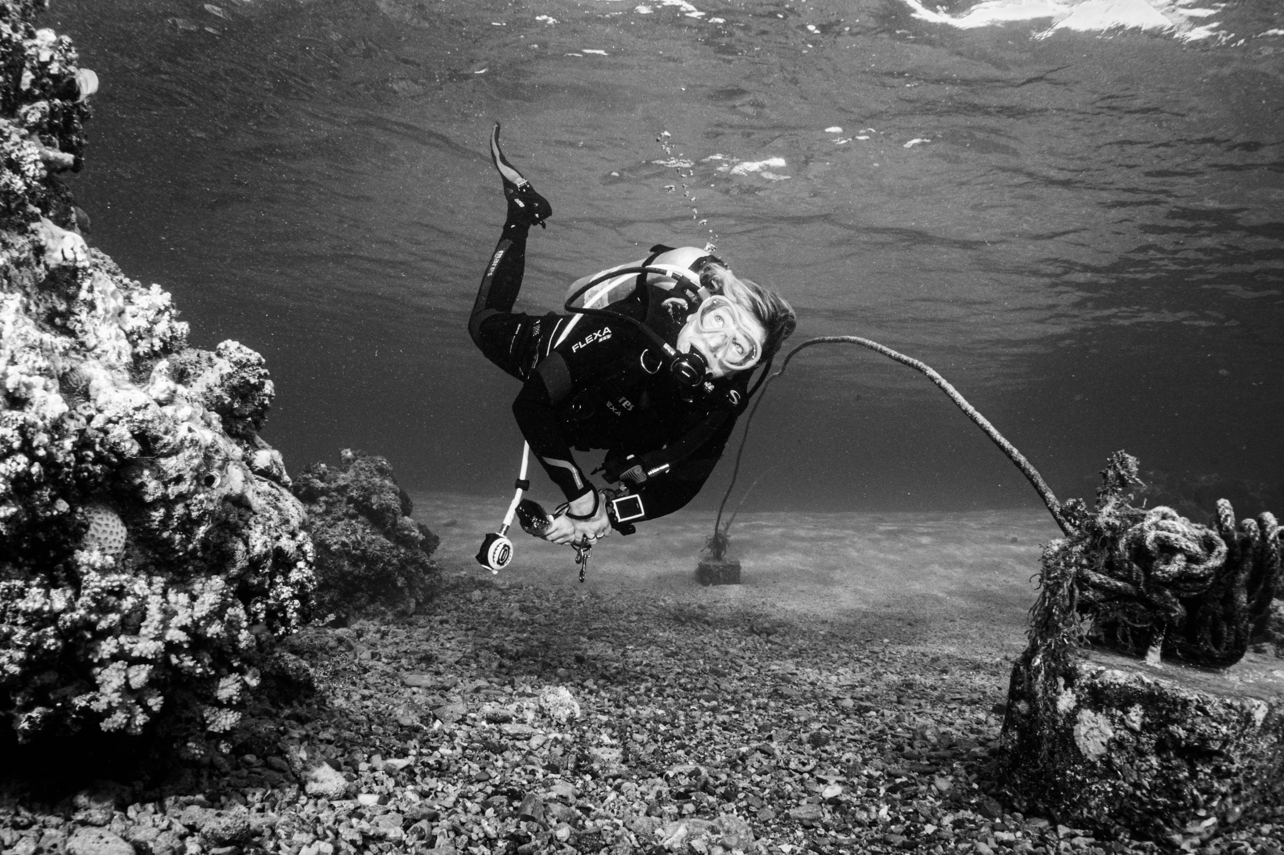 Scuba diver exploring coral reef underwater in black and white photograph.
