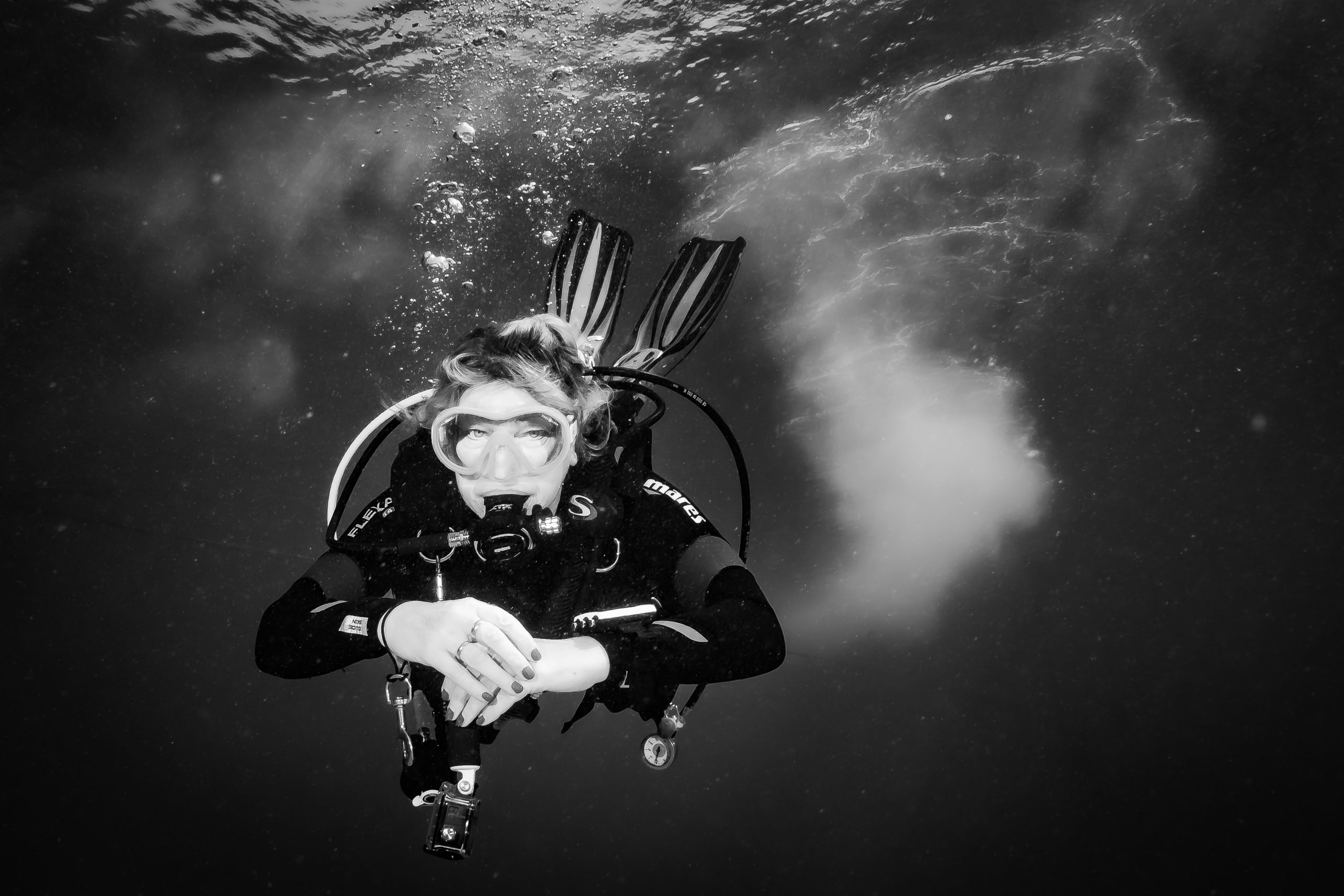 Scuba diver with mask and gear underwater, surrounded by bubbles in a monochrome setting.