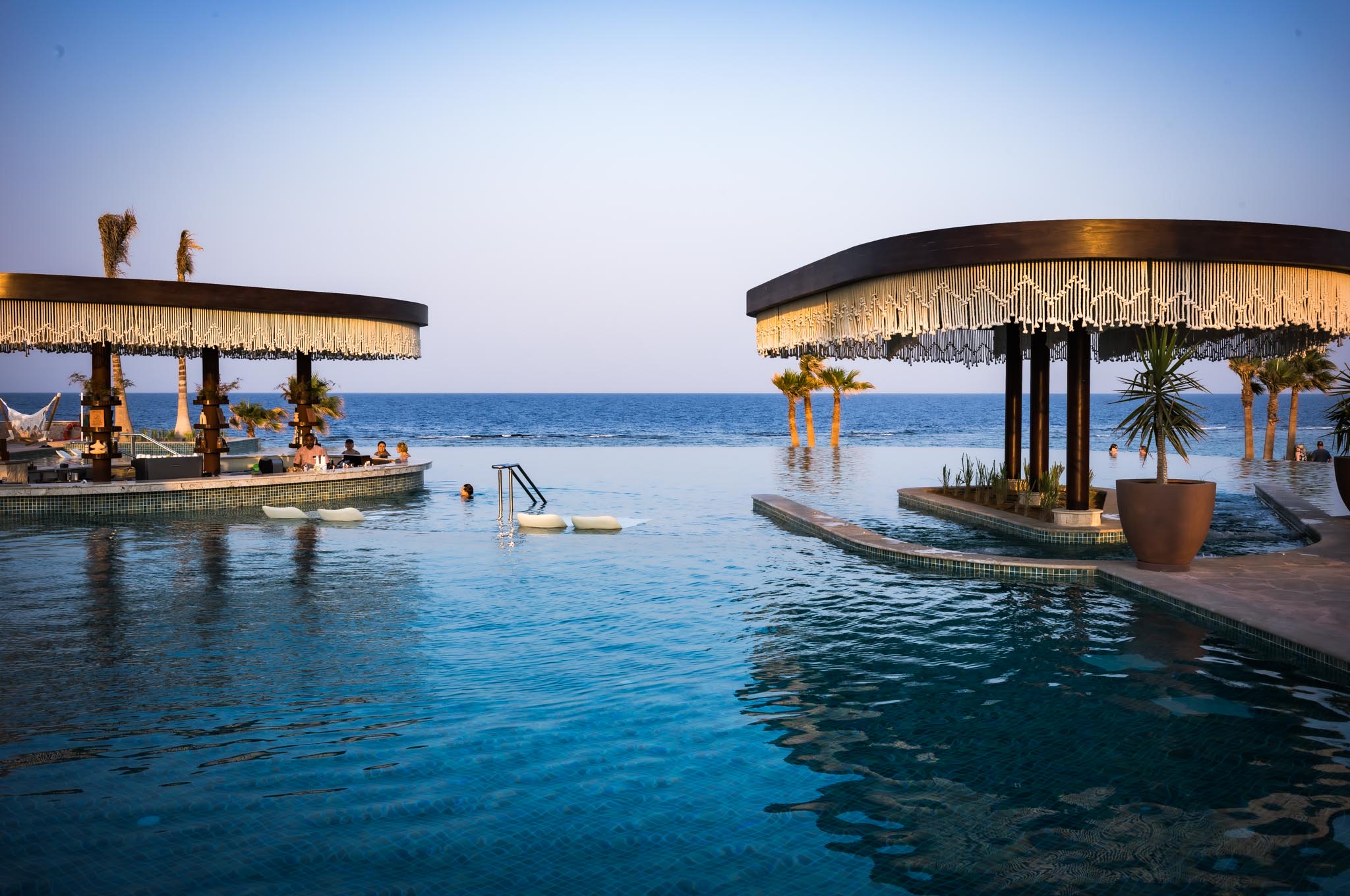 Luxurious beachfront infinity pool with swim-up bar and stunning ocean views at sunset.