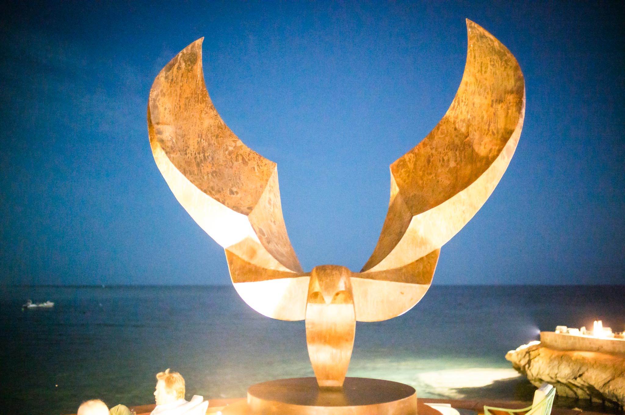 Large bronze eagle sculpture overlooking the ocean at night, under a clear blue sky.