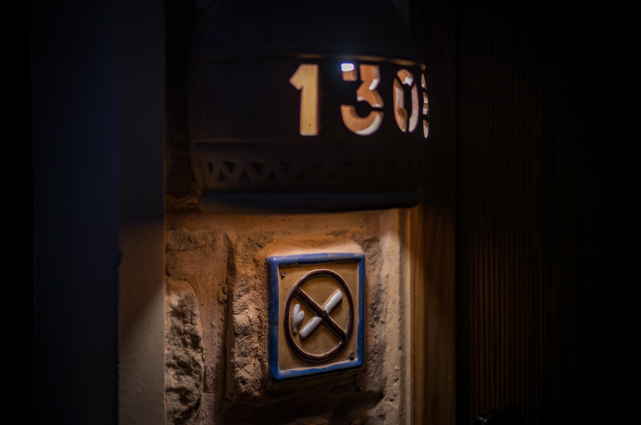 Wall-mounted sign depicts crossed-out cigarettes under house number 1305. Dim lighting creates a warm, cozy feel.
