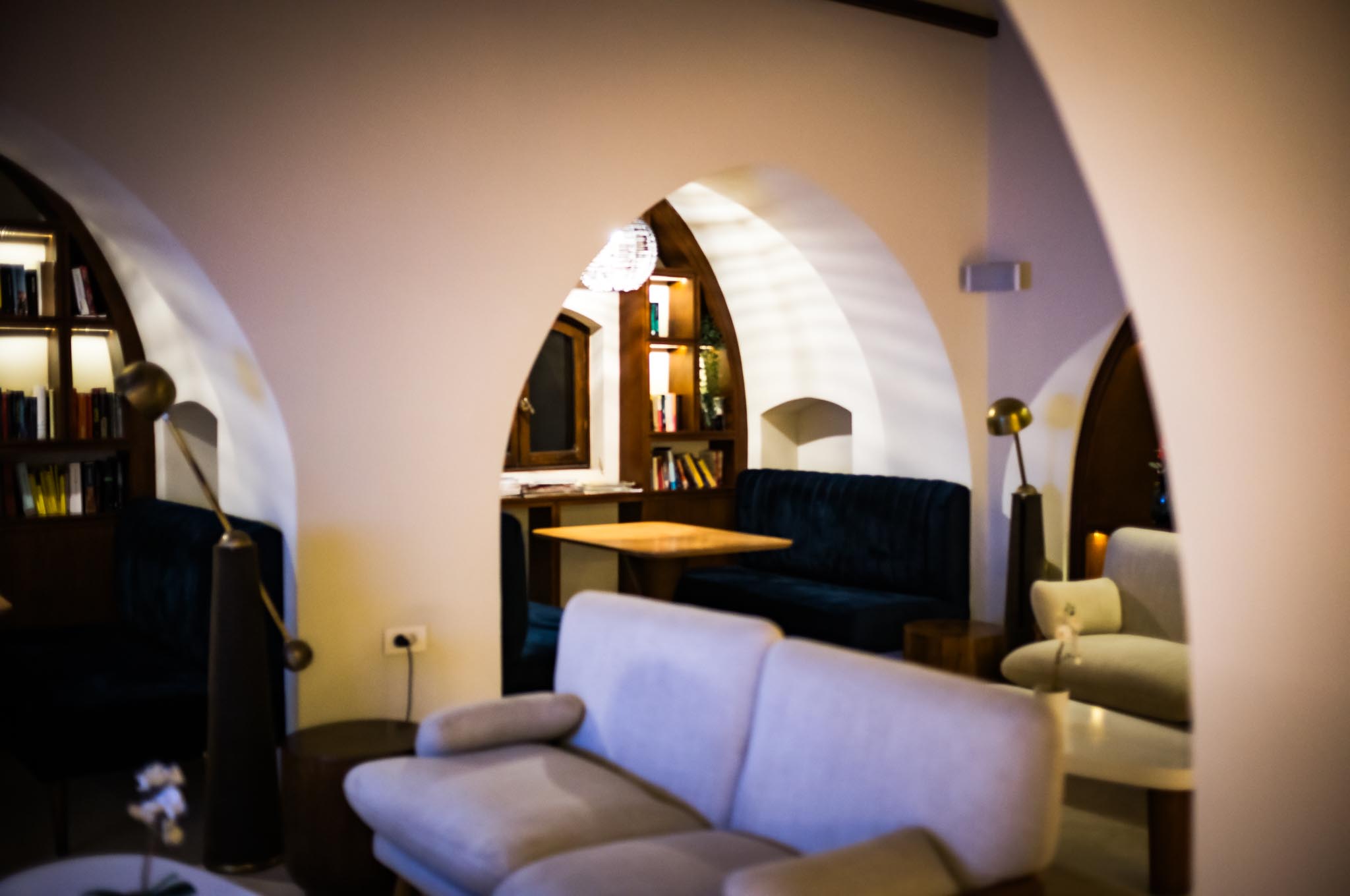 Cozy lounge with arched alcoves, plush sofas, wooden tables, and bookshelves in a warm, inviting atmosphere.