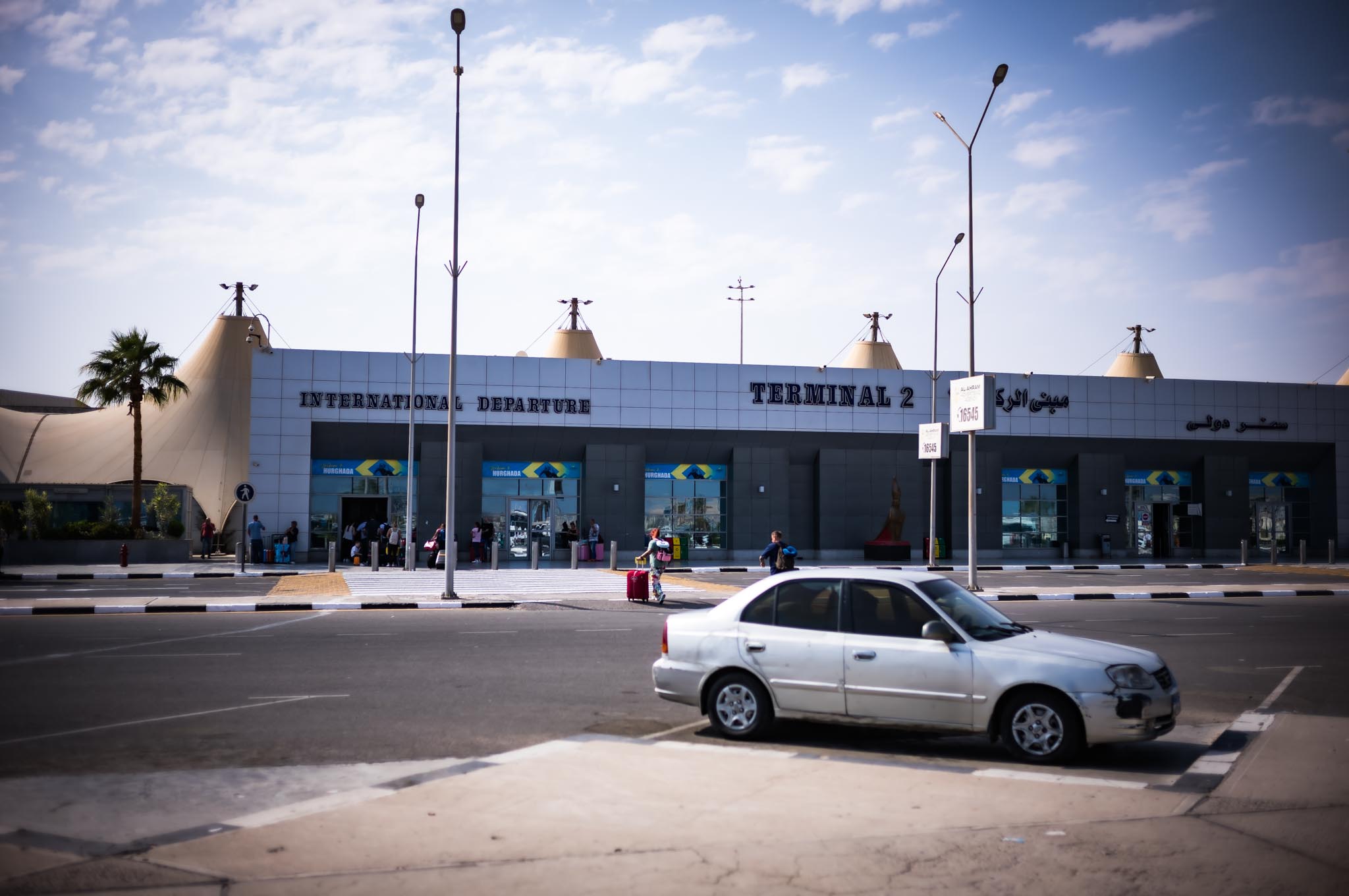 Airport Terminal 2 entrance with cars and travelers, under a clear sky.