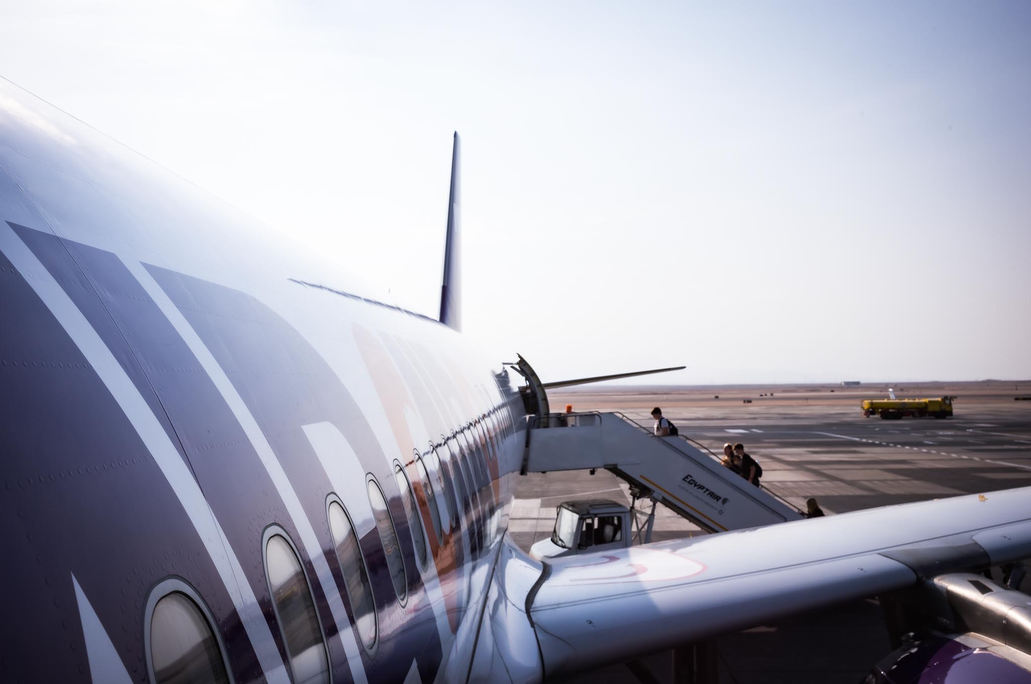 Airplane boarding with passengers on stairs at sunny airport.