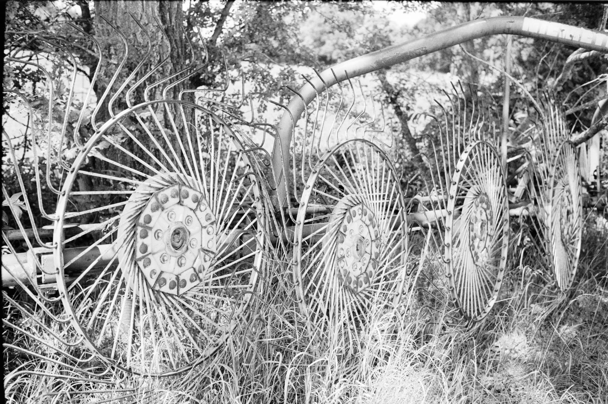 Black and white photo of old farm equipment with large spoked wheels in a grassy area.