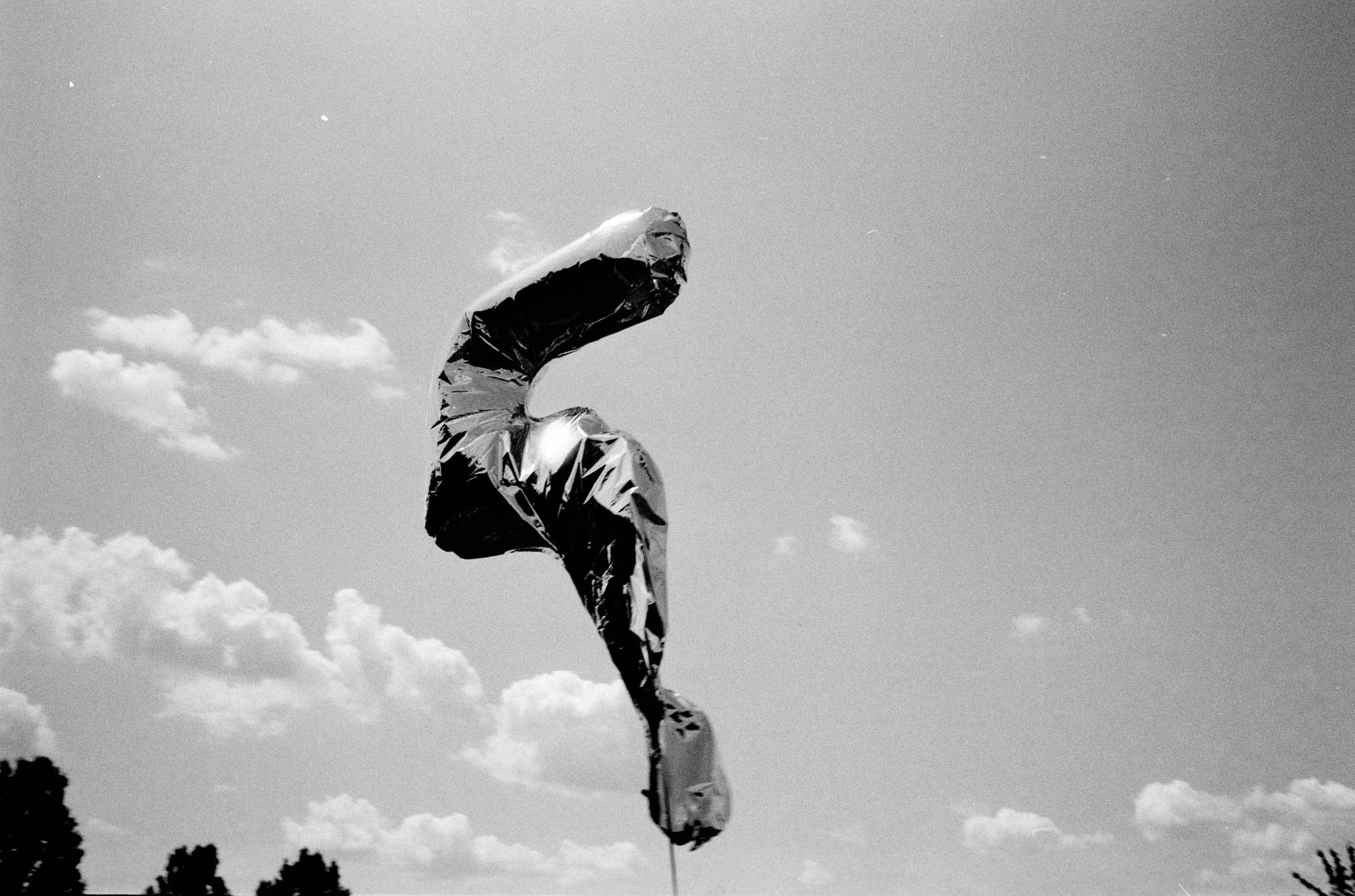 Silver number five balloon floating against a cloudy sky.