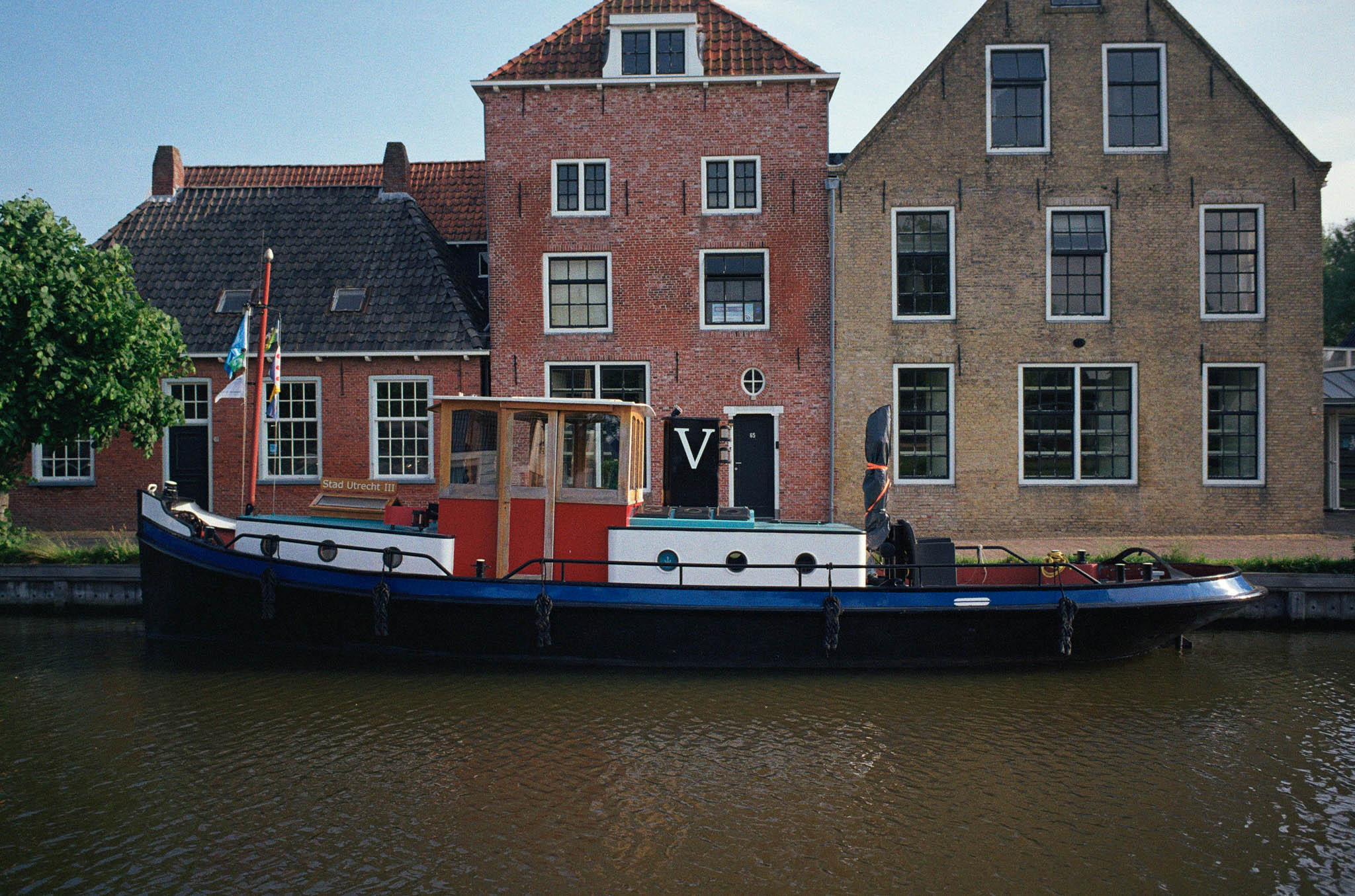 Vintage canal boat moored beside historic brick buildings with tiled roofs in a European cityscape.