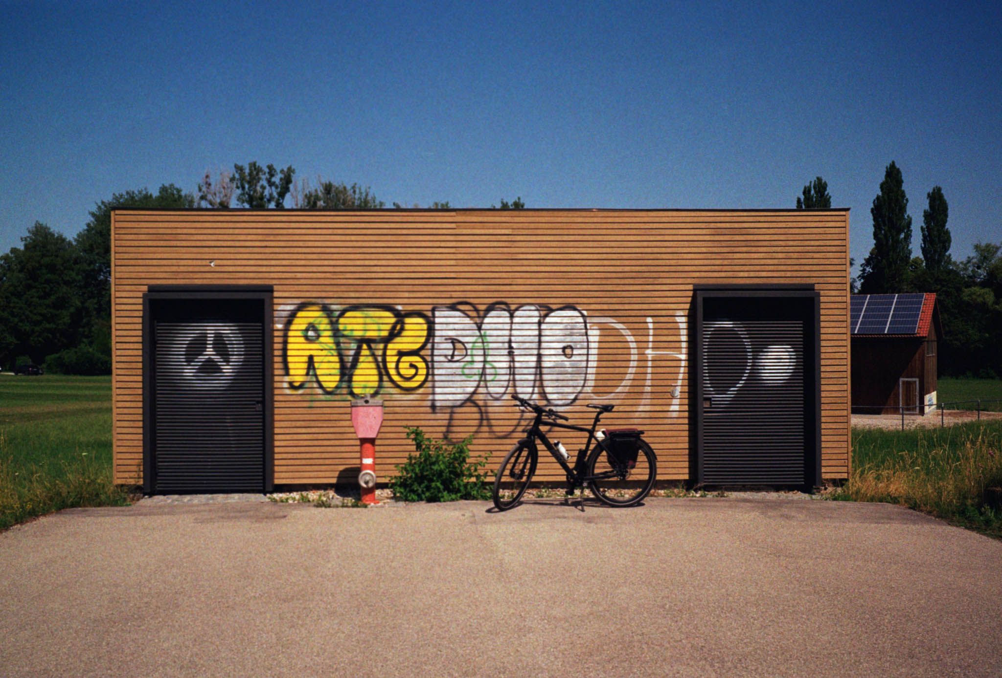Wooden building with colorful graffiti, bicycle parked in front, and solar panels visible on adjacent structure.