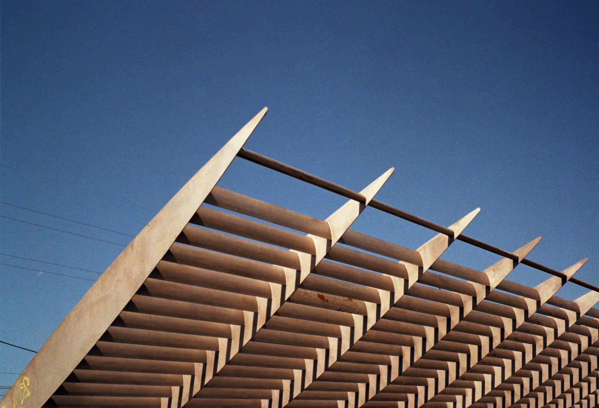 Modern architectural structure with angled beams against a clear blue sky.