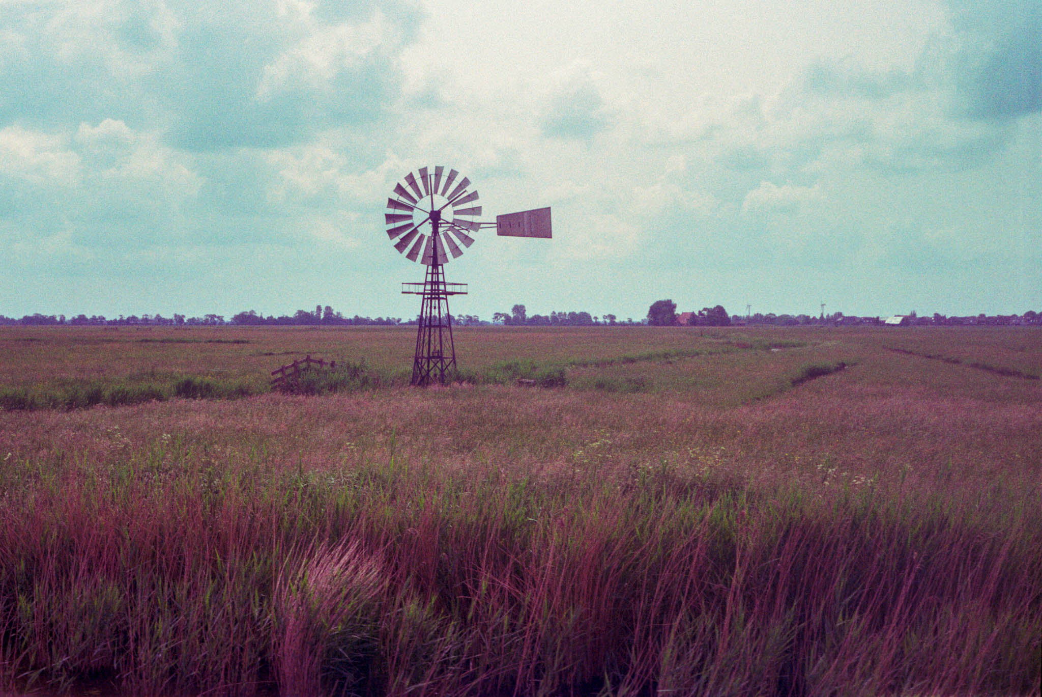 Vintage windmill in a lush, grassy field under a cloudy sky.