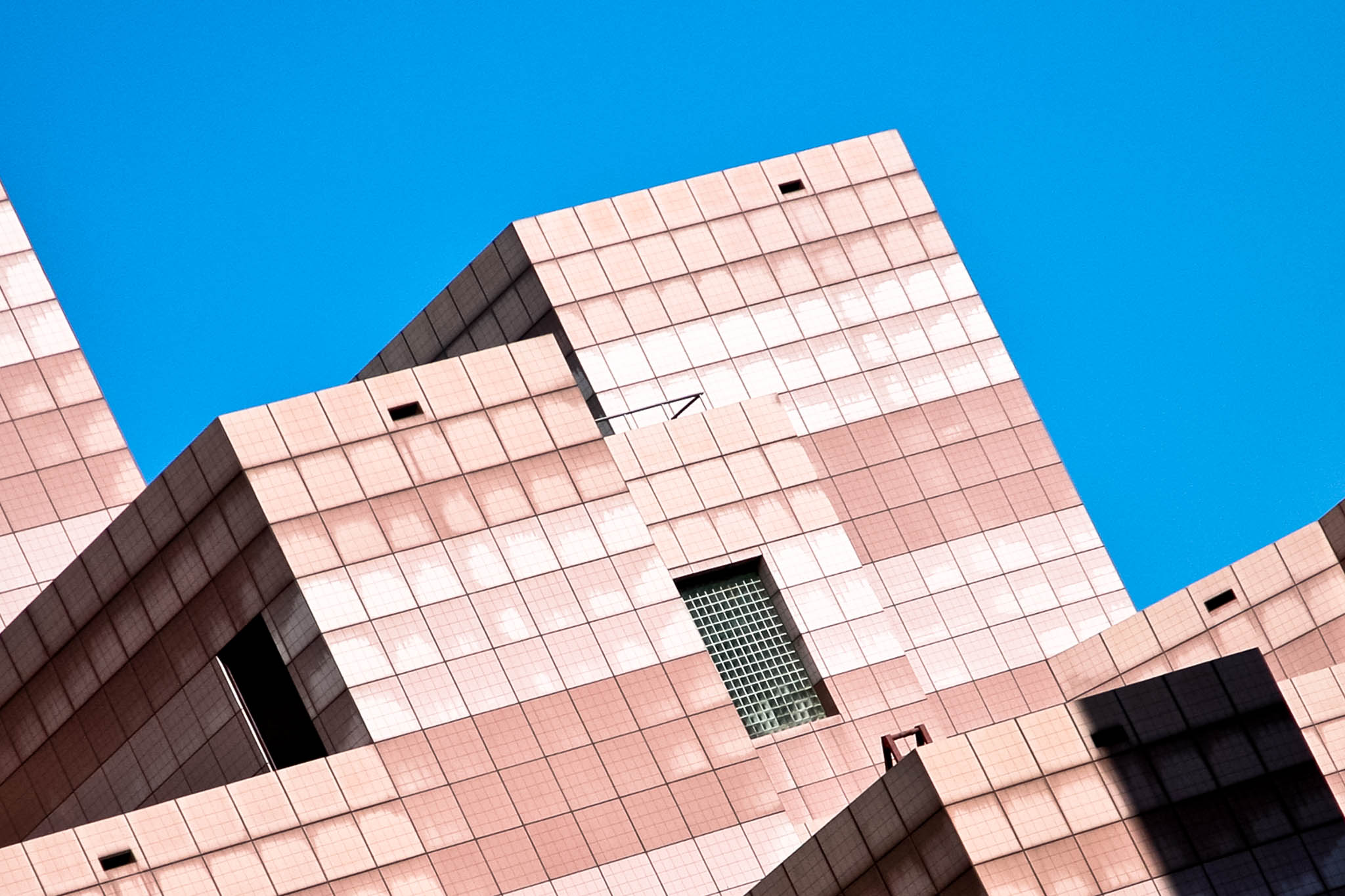 Modern pink-tiled building against clear blue sky, showcasing geometric architecture and window accents.