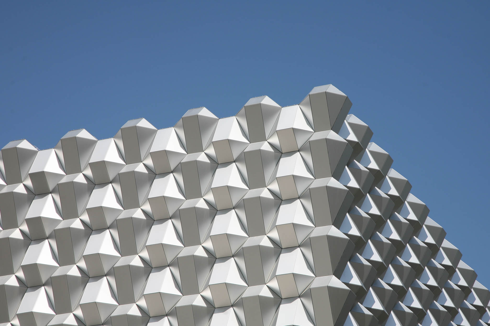 Futuristic building facade with geometric, silver 3D panels against a clear blue sky.