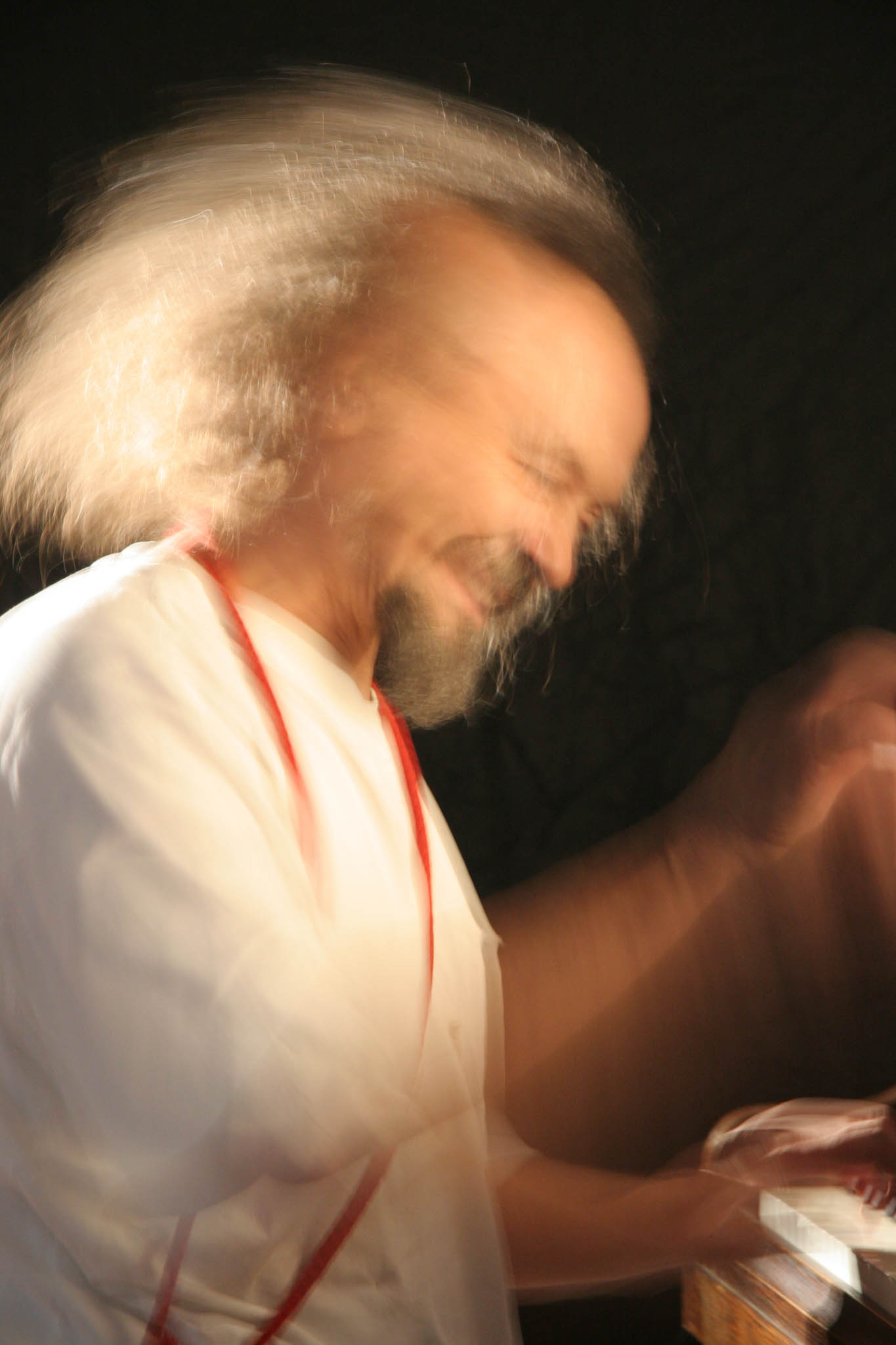 Blurry motion image of a joyful man in a white shirt playing percussion with dramatic lighting.