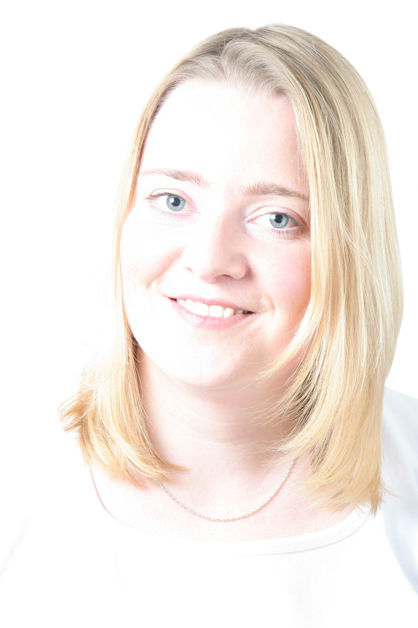 Smiling woman with blonde hair and blue eyes wearing a white shirt against a bright background.