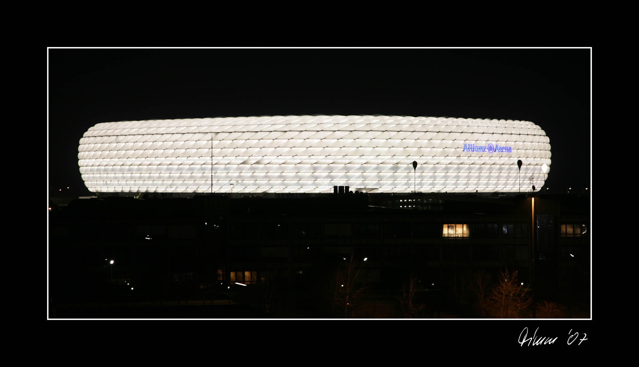 Illuminated Allianz Arena stadium at night, featuring its iconic diamond-shaped facade against the dark sky.
