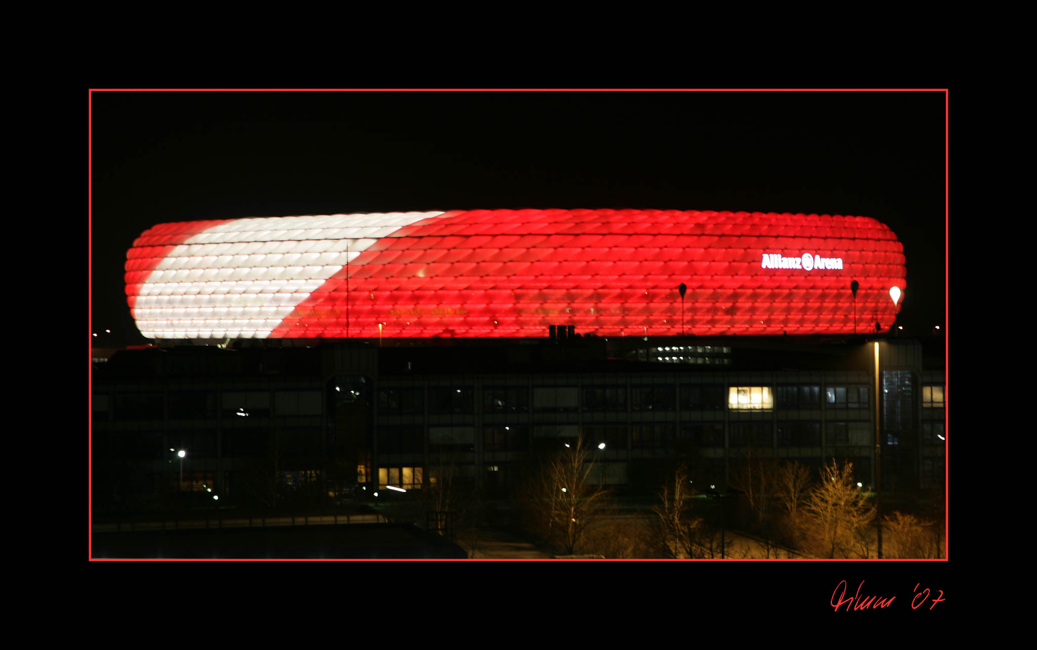 Red and white illuminated Allianz Arena at night, vibrant exterior lights, stadium in dark surroundings.