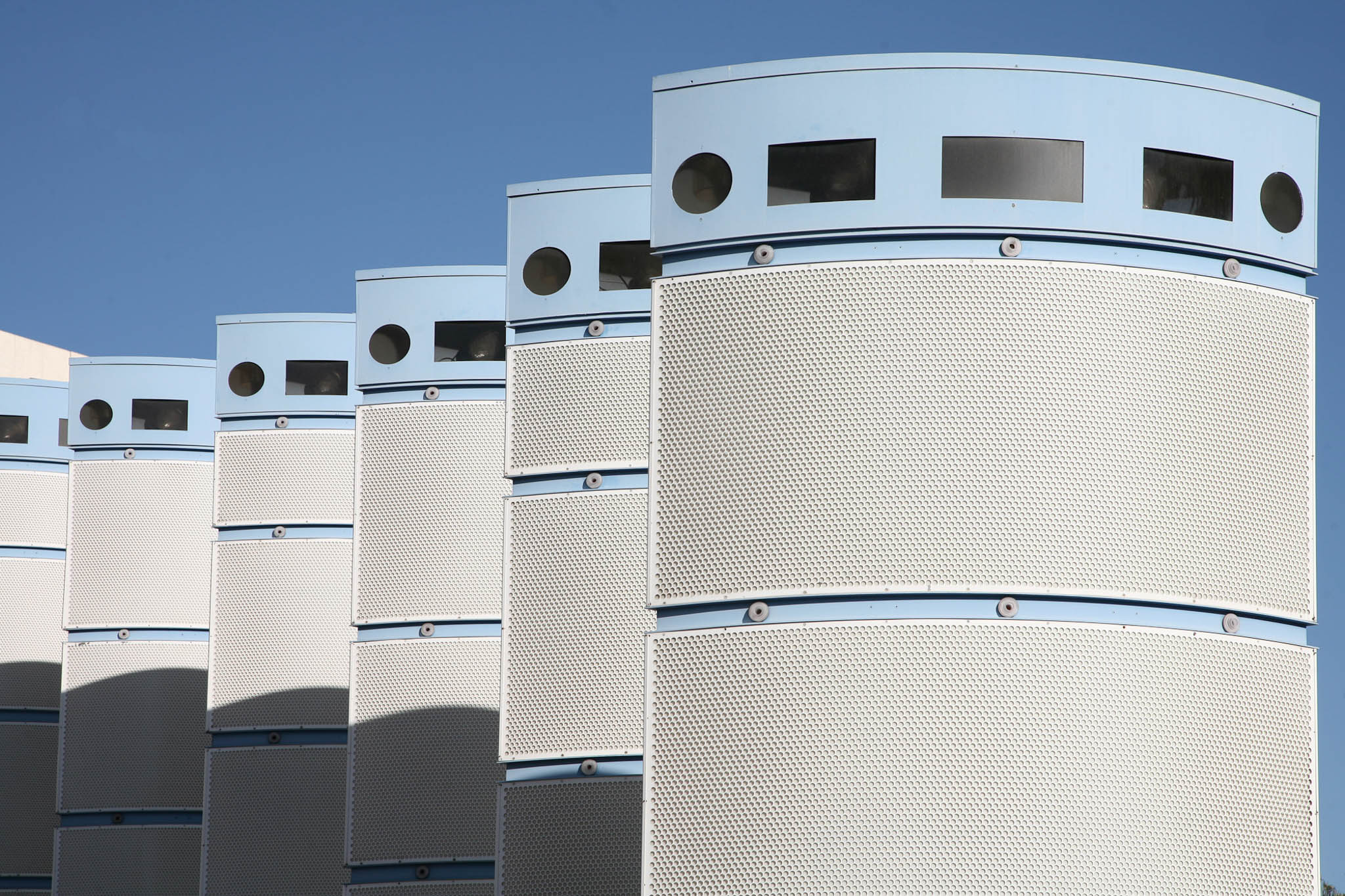 Modern architectural building with curved, perforated facades and blue accents under a clear blue sky.