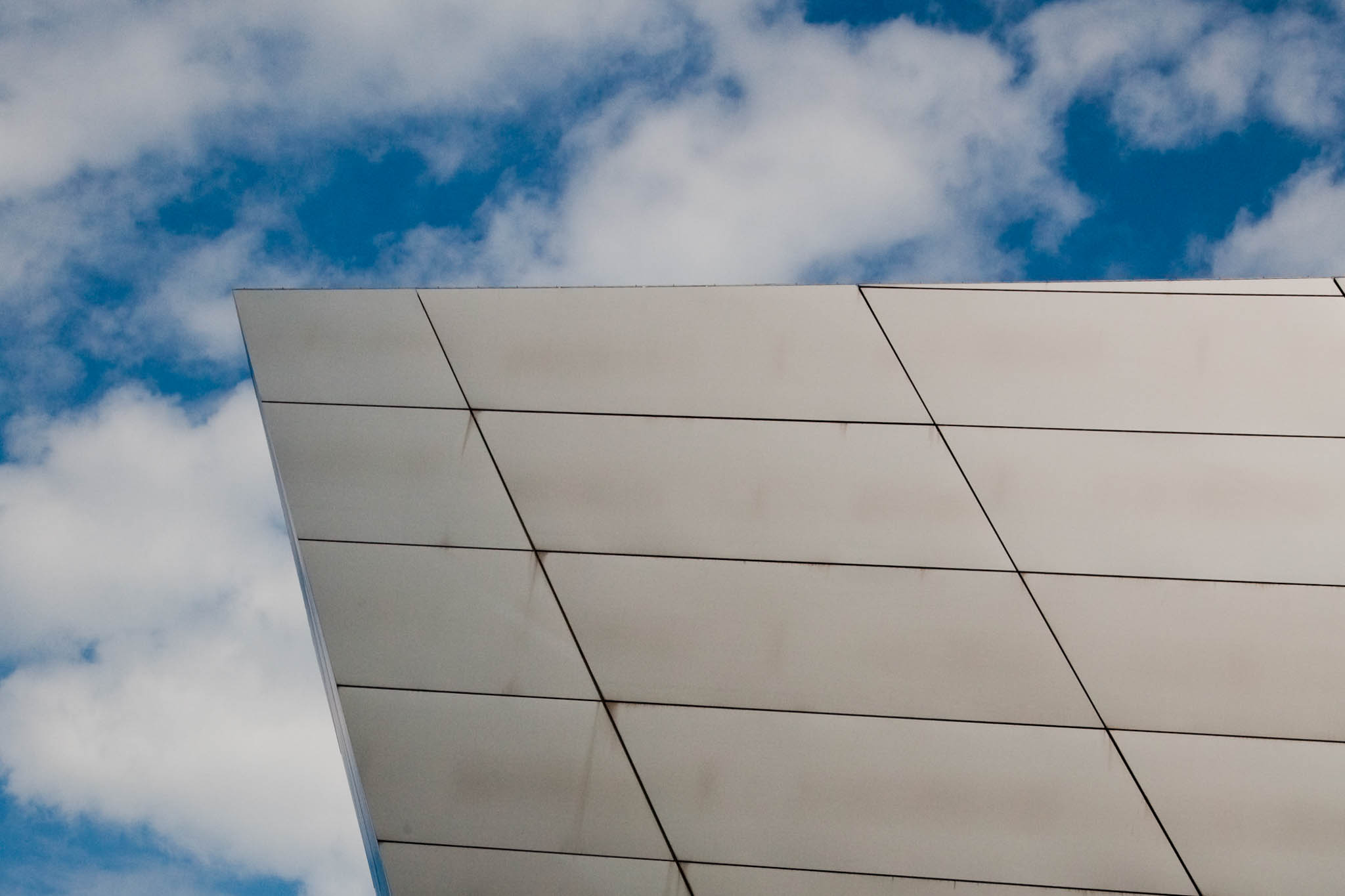 Modern building with angular metal facade against a blue sky with clouds.