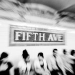 Blurred motion image of people sitting by a Fifth Ave subway sign, creating an abstract, dynamic effect.