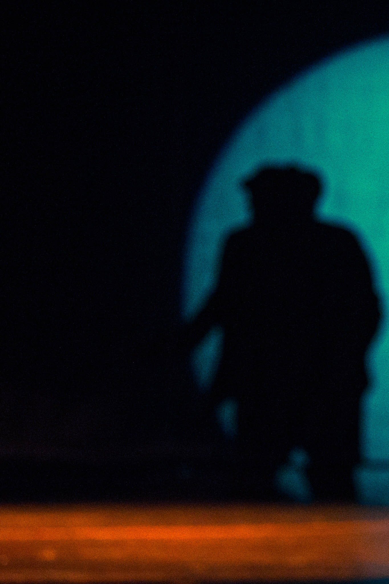 Silhouette of a person against a blue-green circular light on stage, with orange hues at the bottom.