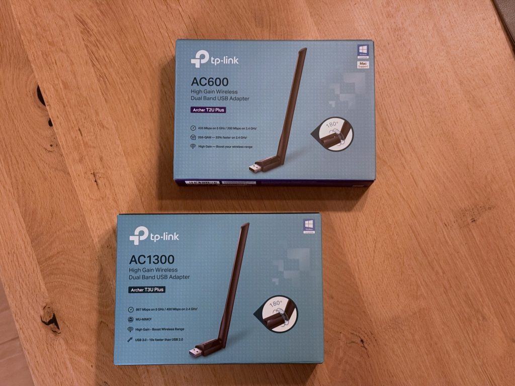 Two TP-Link Wi-Fi USB adapters (AC600, AC1300) boxes on a wooden table, showcasing high-gain dual-band capabilities.