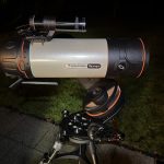 Celestron telescope on a tripod under night sky, set on a garden patio for stargazing.