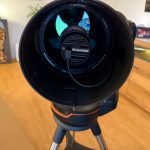 Unboxing Celestron Origin Mark II – and Surviving the Firmware Update Telescope interior view in cozy room with wooden floor, shelf of firewood, and TV screen in the background.